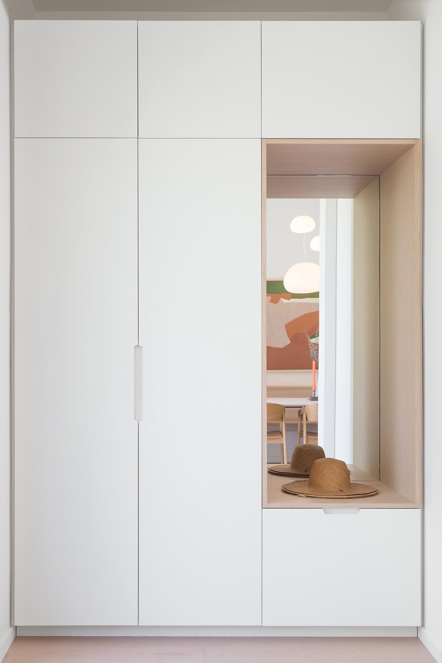 This modern entryway showcases Ash wood floors and a closet with a lacquered white finish and a small bench with a mirror.