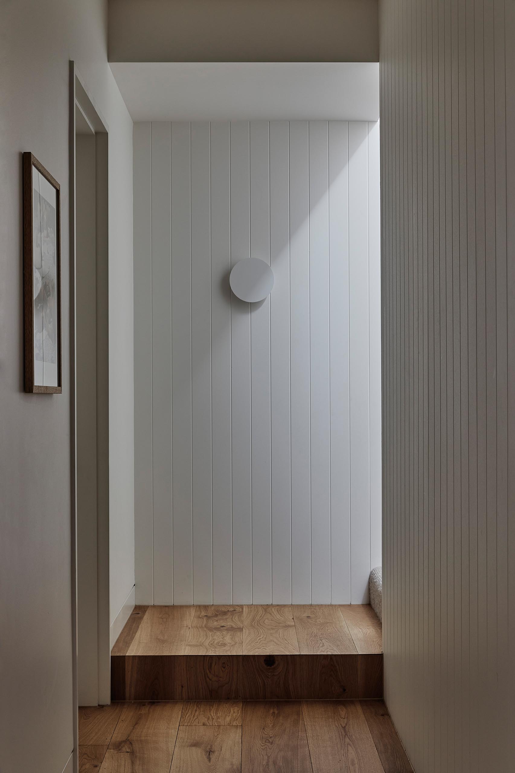 A modern hallway with wood flooring and white paneled walls.