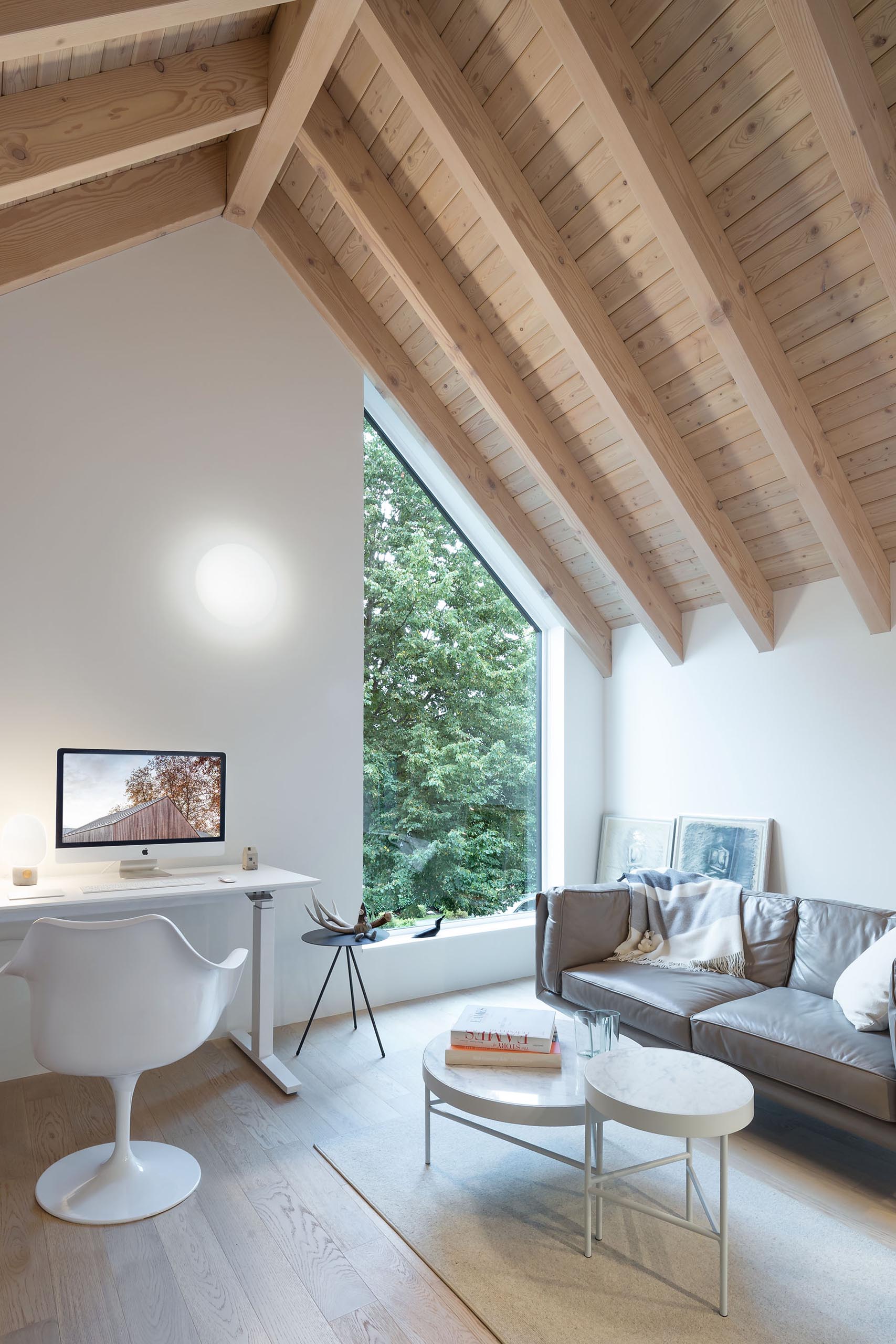 This modern home office includes white walls and a vaulted timber ceiling.