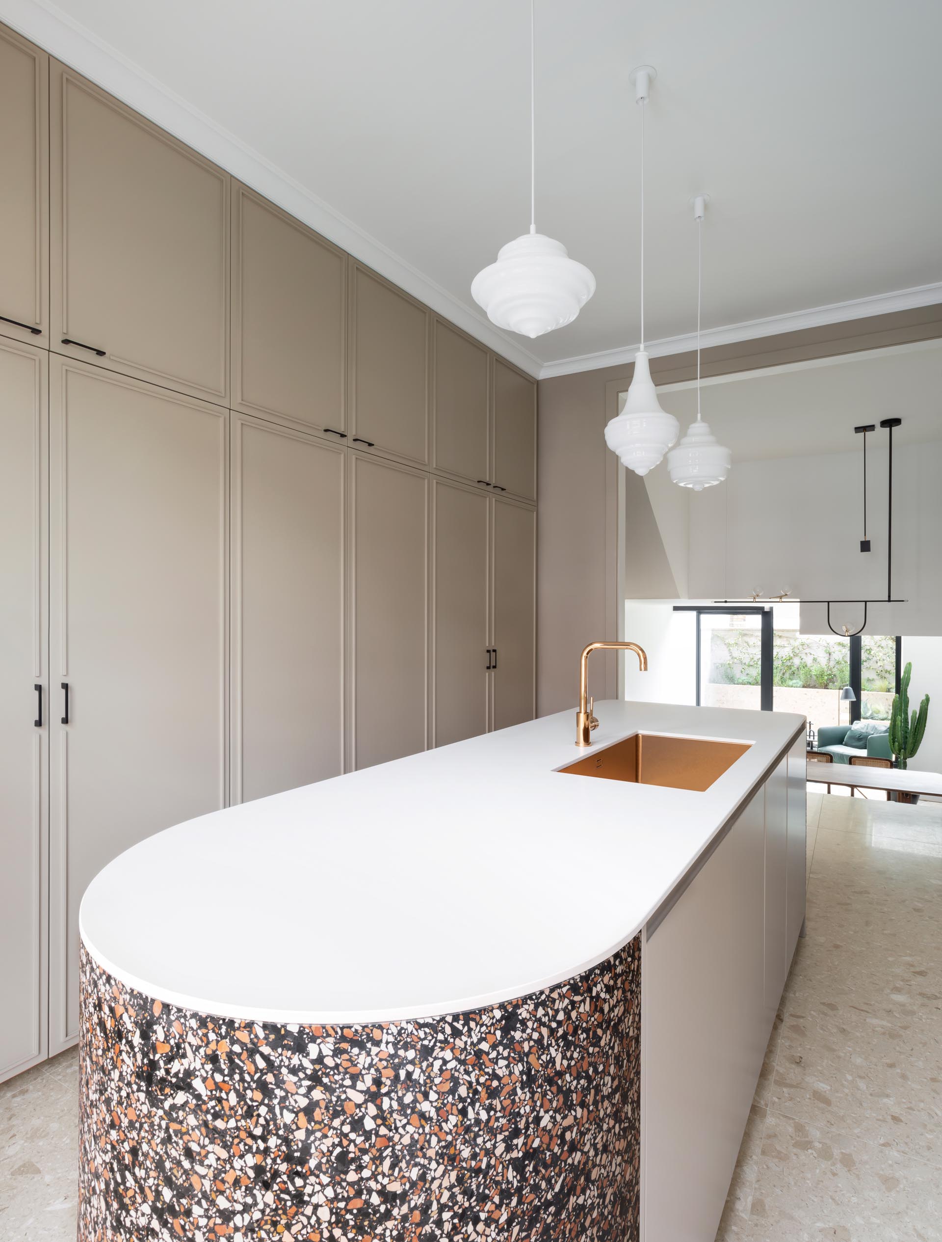A modern kitchen with tan cabinets, white countertops, and a terrazzo accent.