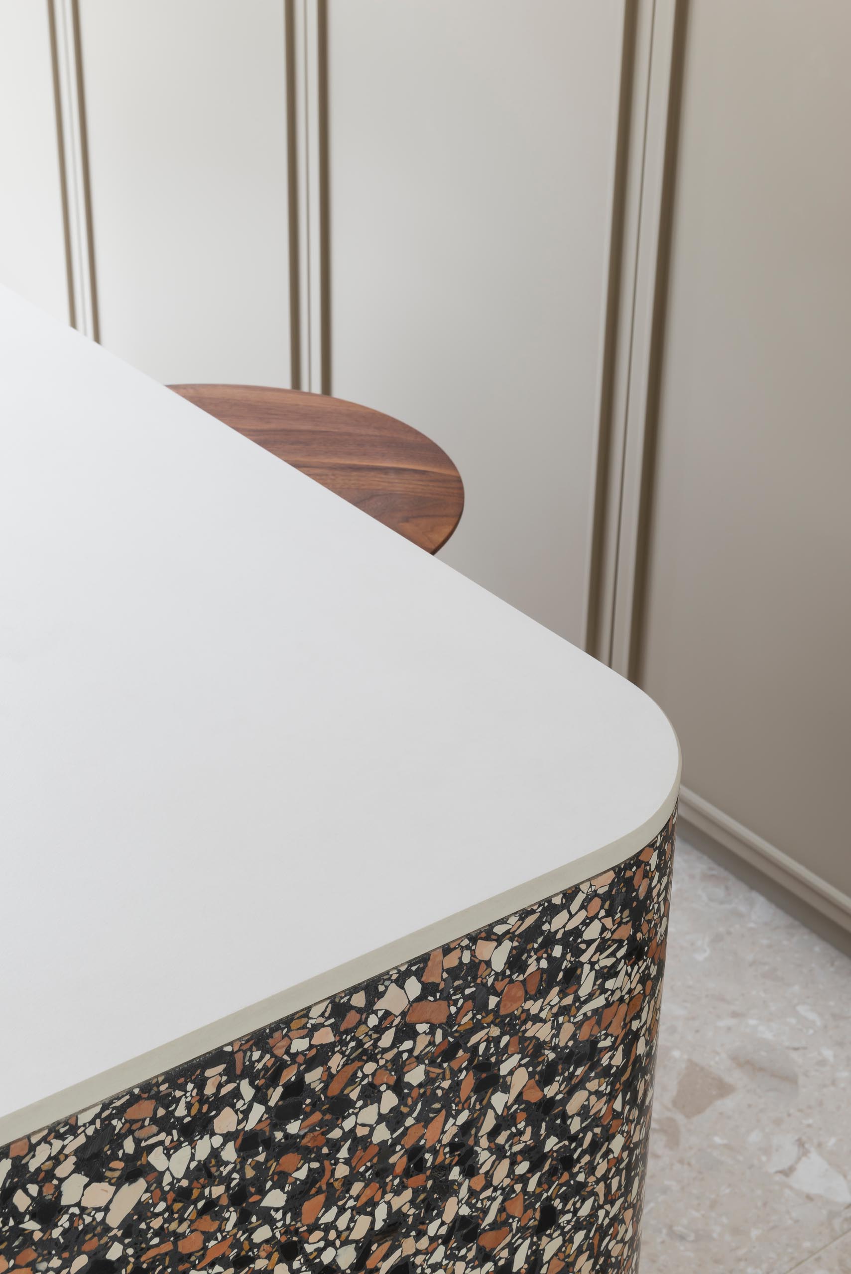 A modern kitchen with tan cabinets, white countertops, and a terrazzo accent.