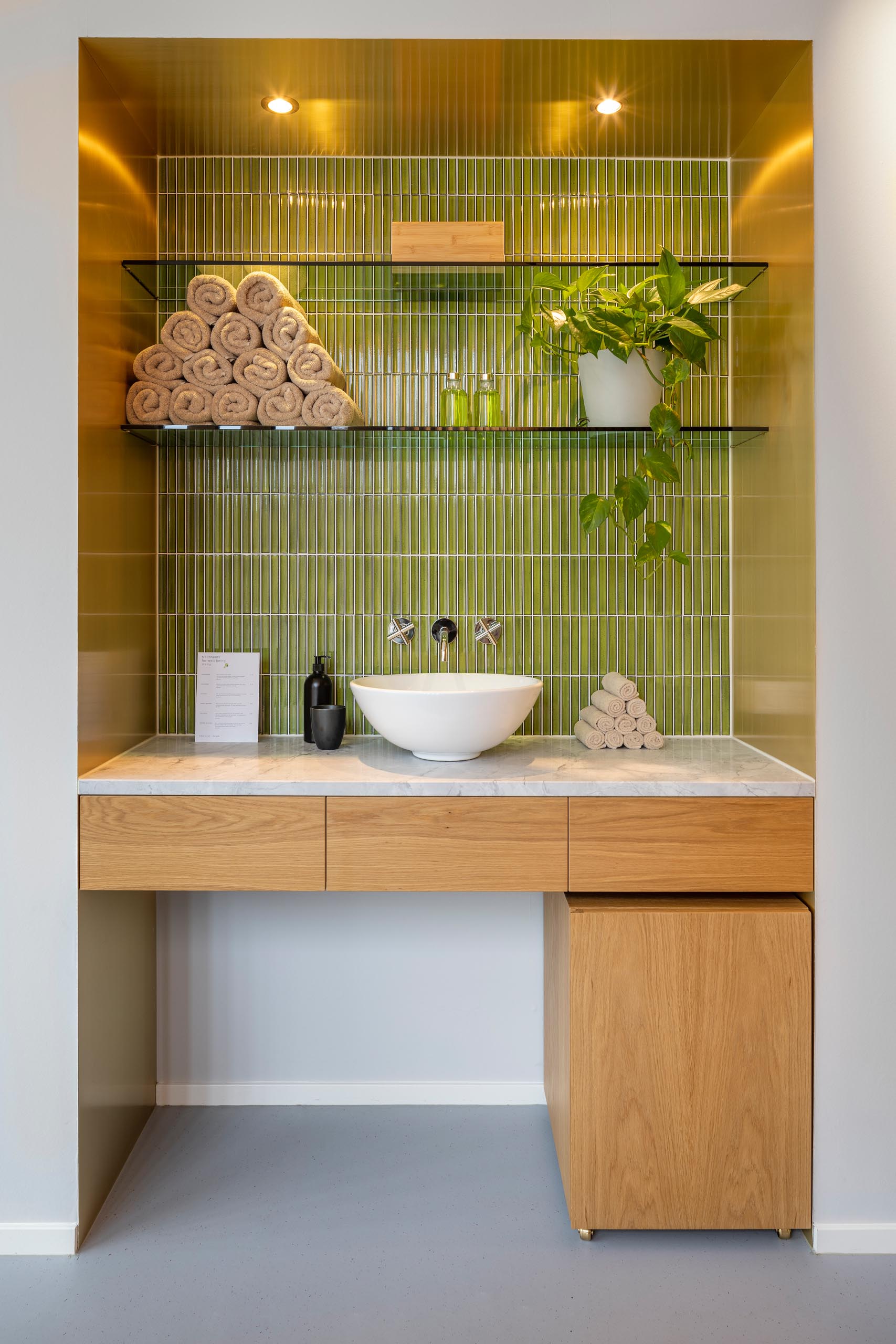 Green, rectangular tiles and soft green glass shelves in the brass clad niche.