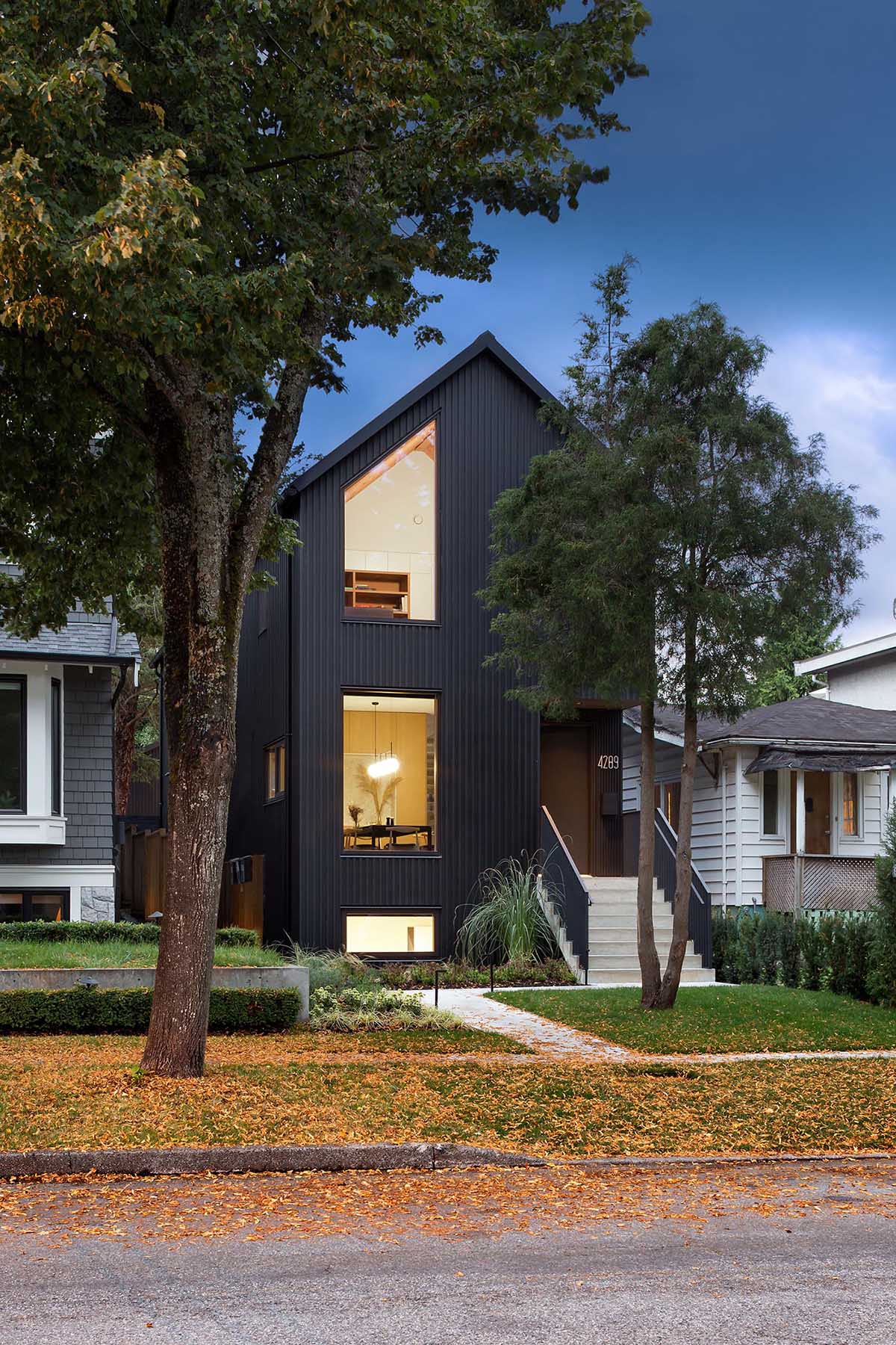 This modern house is clad in narrow board and batten siding with a black finish, and has a matching metal standing seam roof that's sloped.