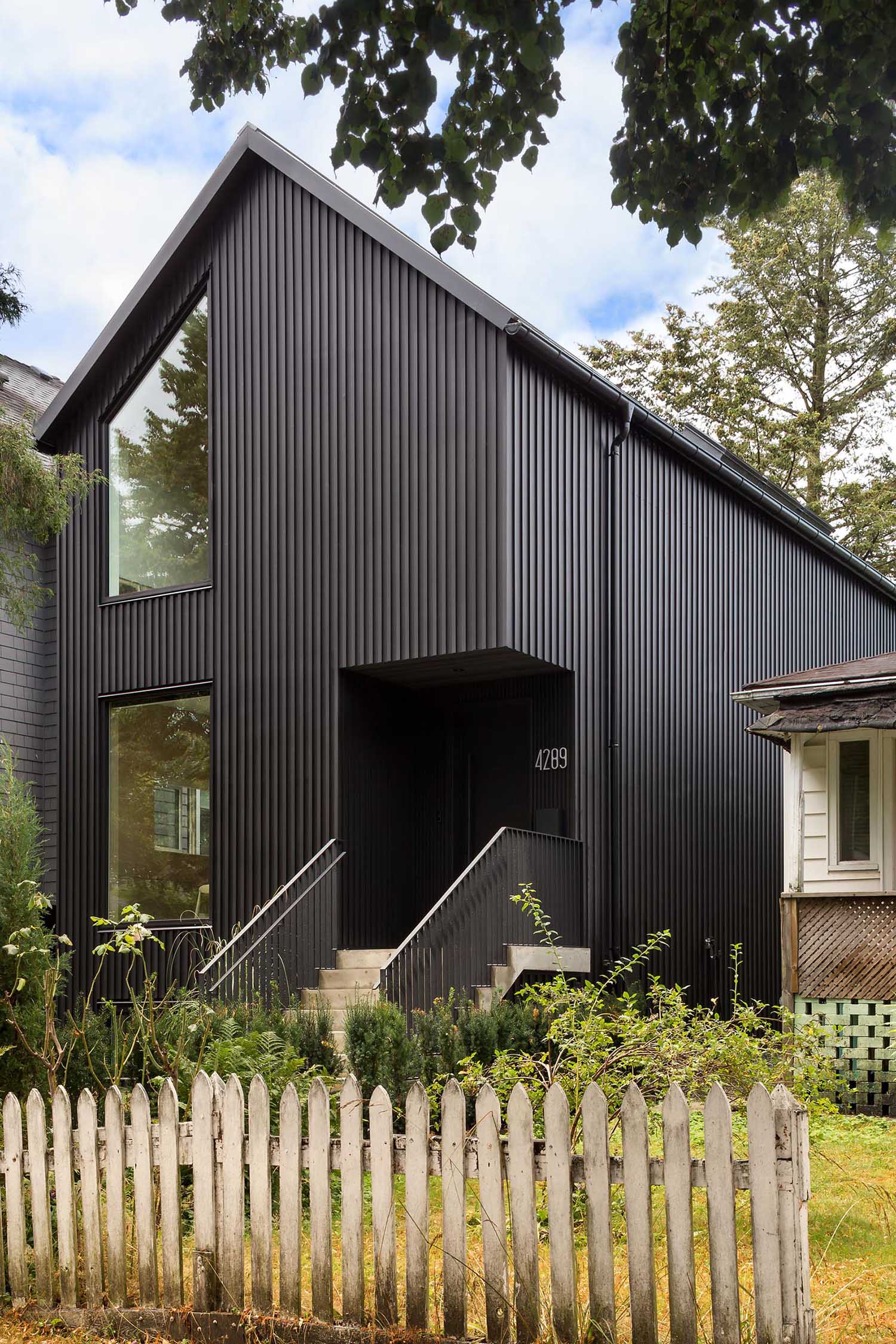 This modern house is clad in narrow board and batten siding with a black finish, and has a matching metal standing seam roof that's sloped.