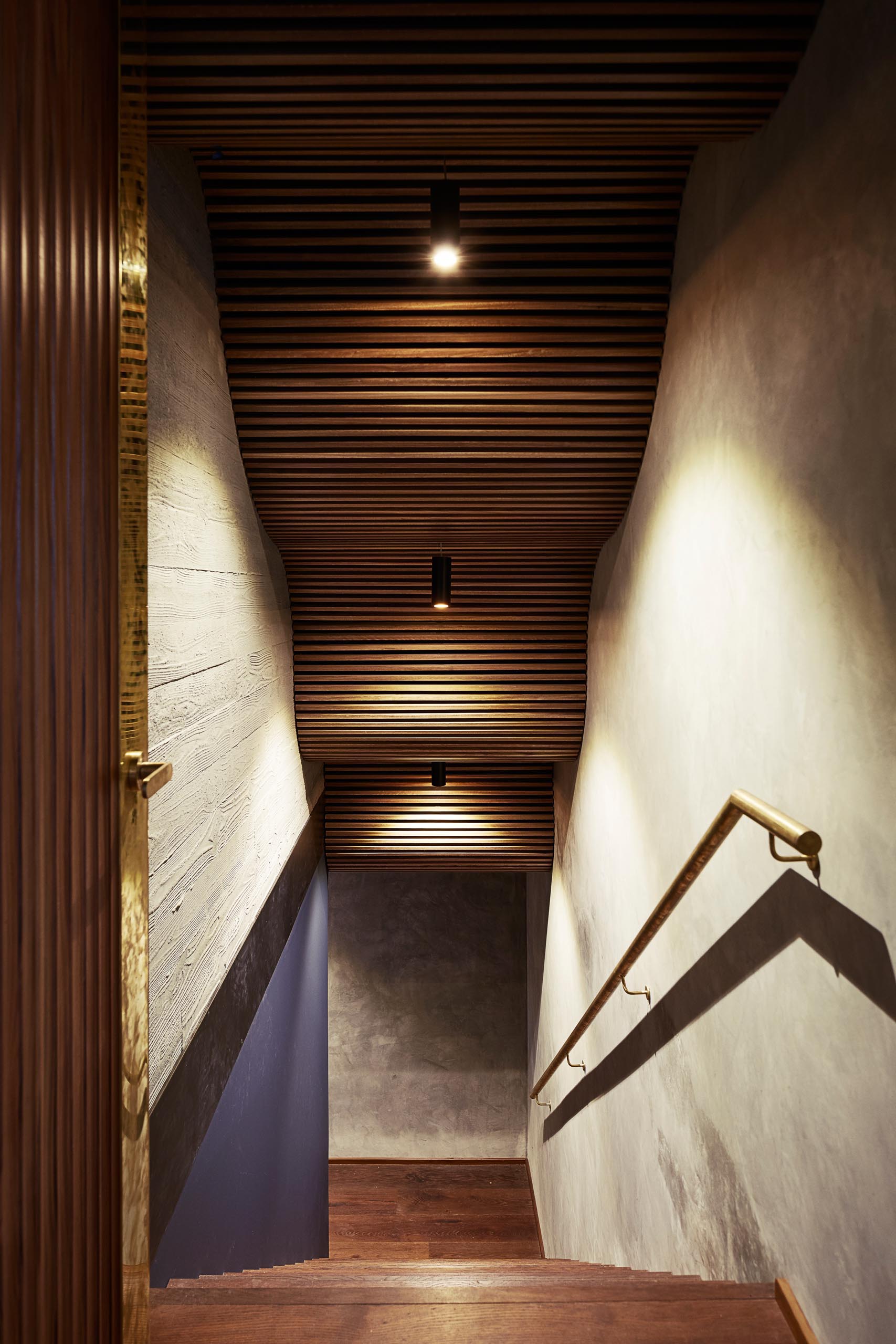 A modern home with stairs that showcase wood detailing, a brass handrail, and board formed concrete walls.