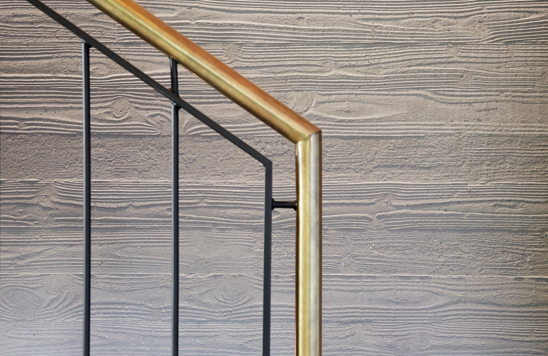 A modern home with wood stairs that showcase a brass handrail and board formed concrete walls.