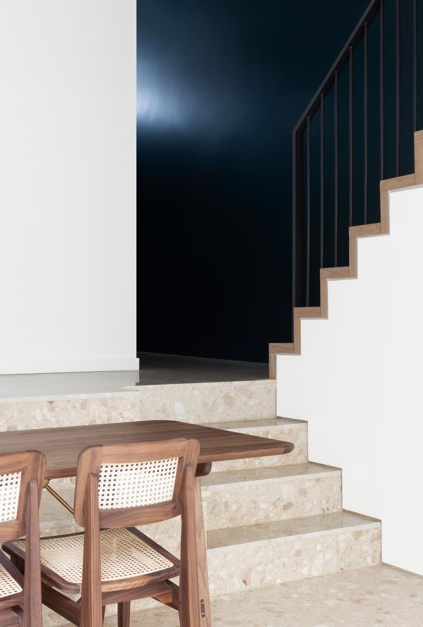 A dark and dramatic staircase with a custom-designed handrail that includes a Terrazzo accent.