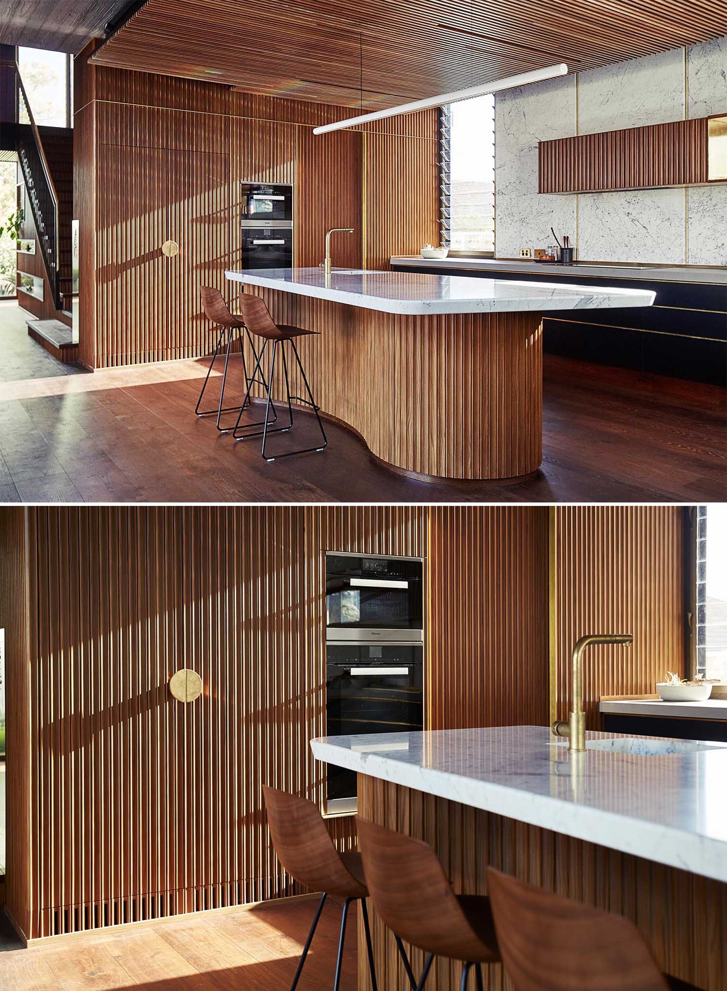 This modern kitchen has an island with a solid marble slab countertop and organically shaped timber cabinetwork. Timber ceilings conceal acoustic insulation.