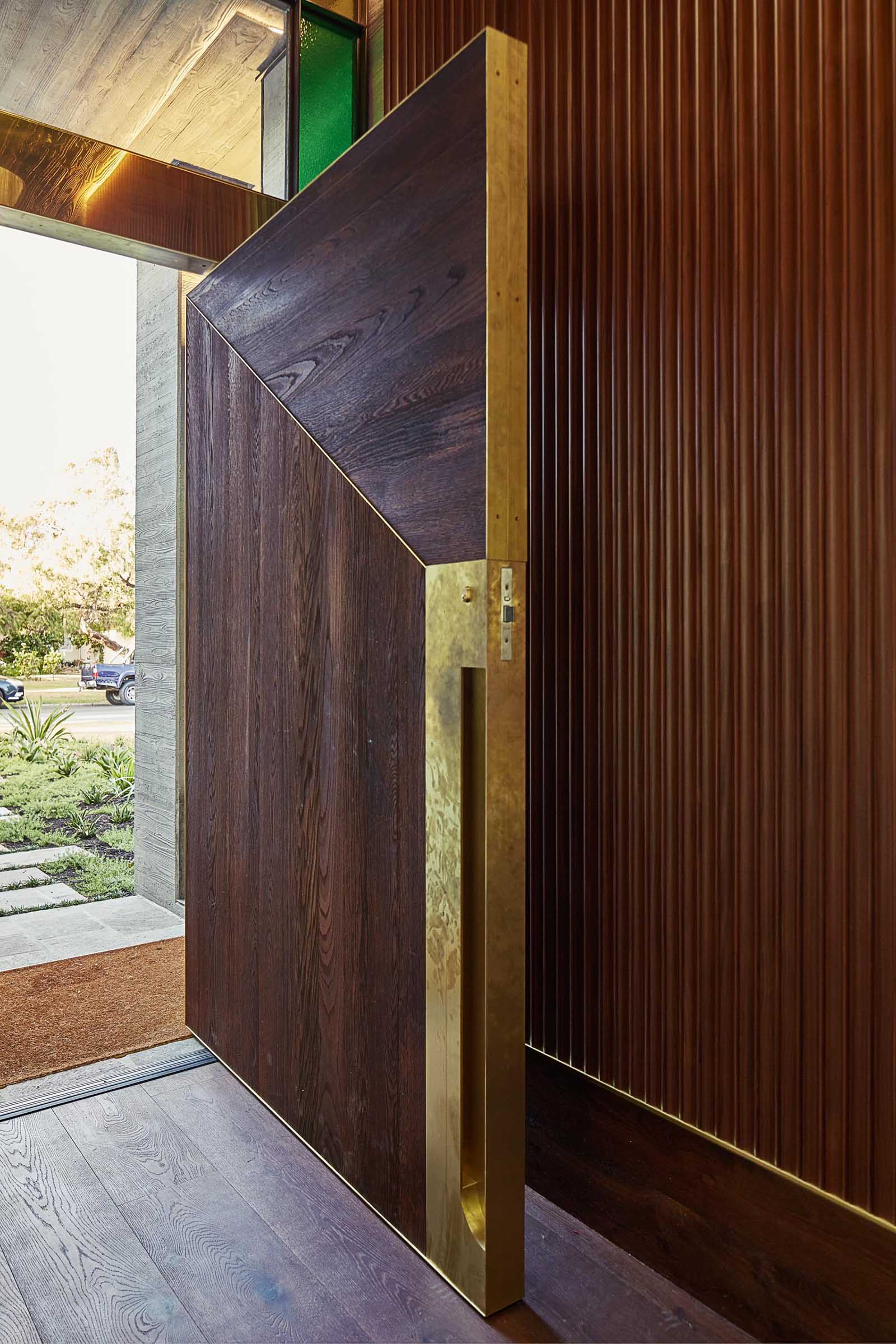 This The timber and brass clad pivoting front door has a custom designed brass door handle.