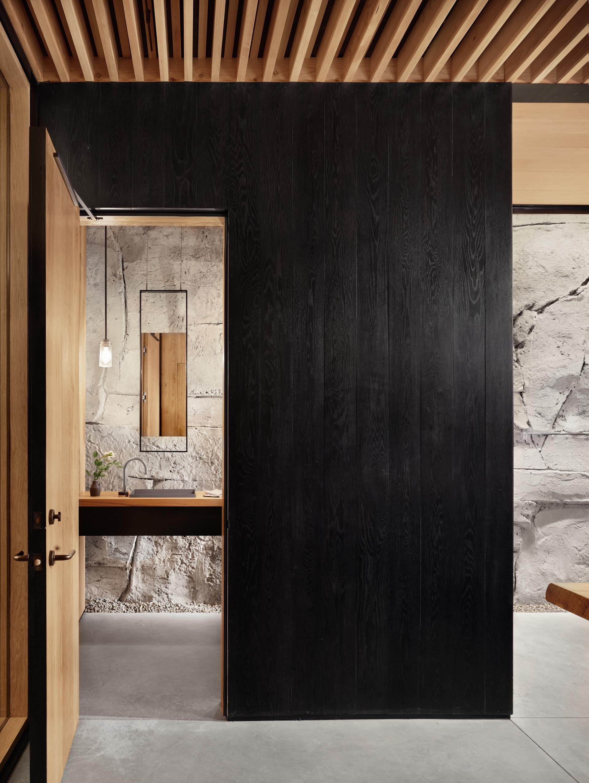 A bathroom hidden within an ebonized wood box includes a floating vanity and hanging mirror.