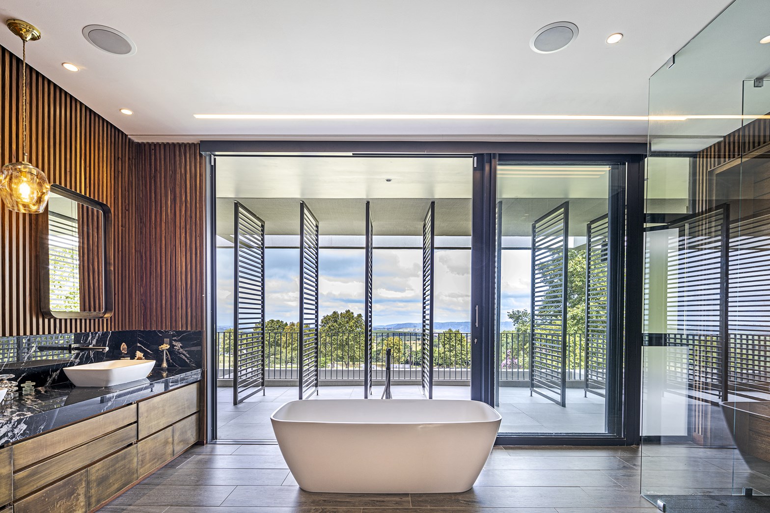 A modern bathroom showcasing wood slat walls, a glass enclosed shower, and a freestanding bathtub.