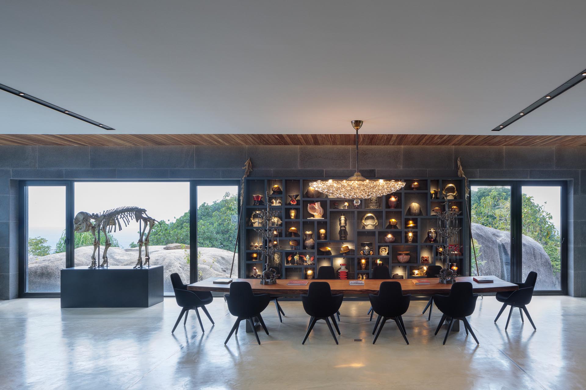 The open plan dining room of this modern house features design elements like concrete floors, oversized furniture, and custom built-in shelving.