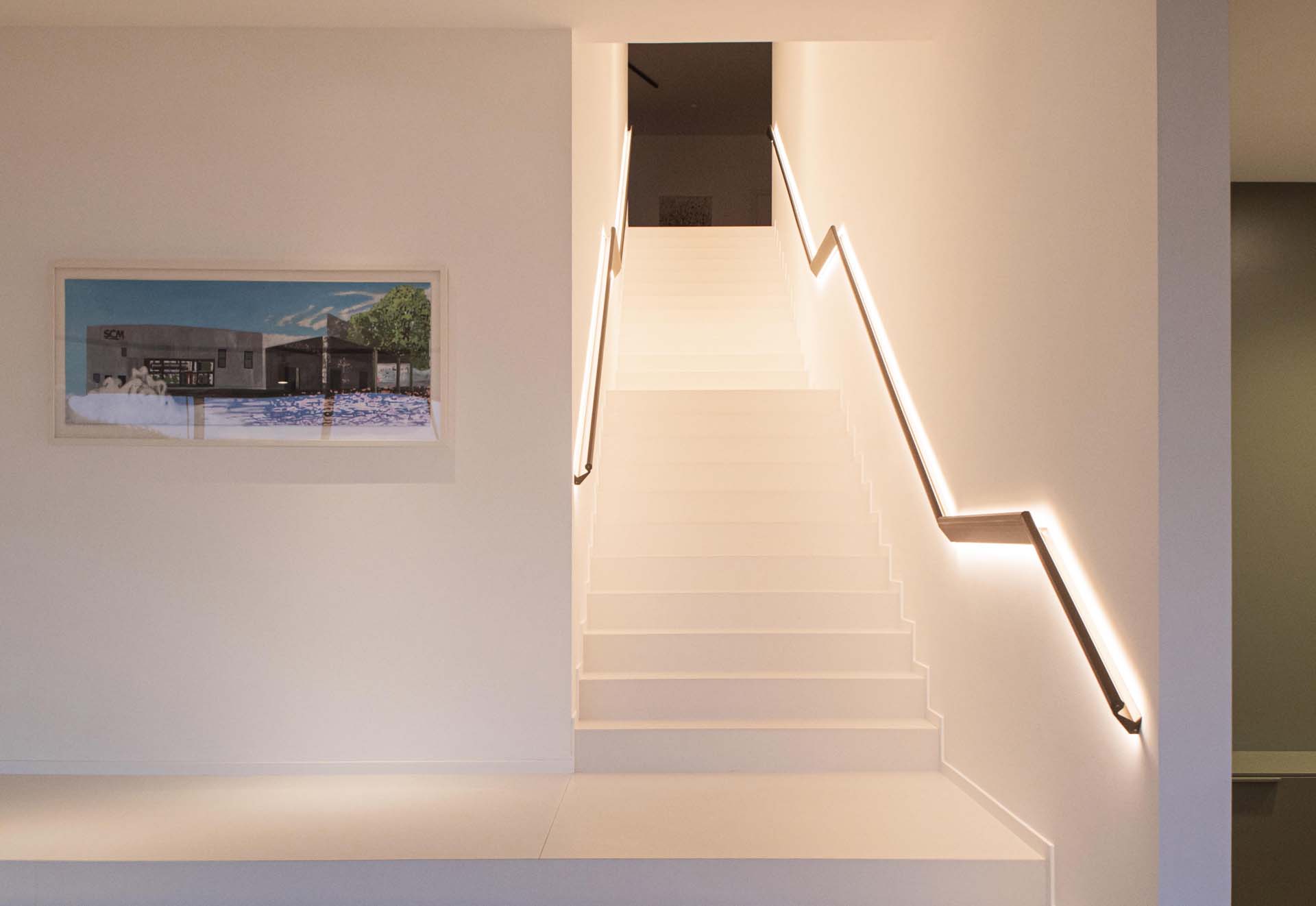 A modern handrail with hidden lighting that casts onto the wall and floor.