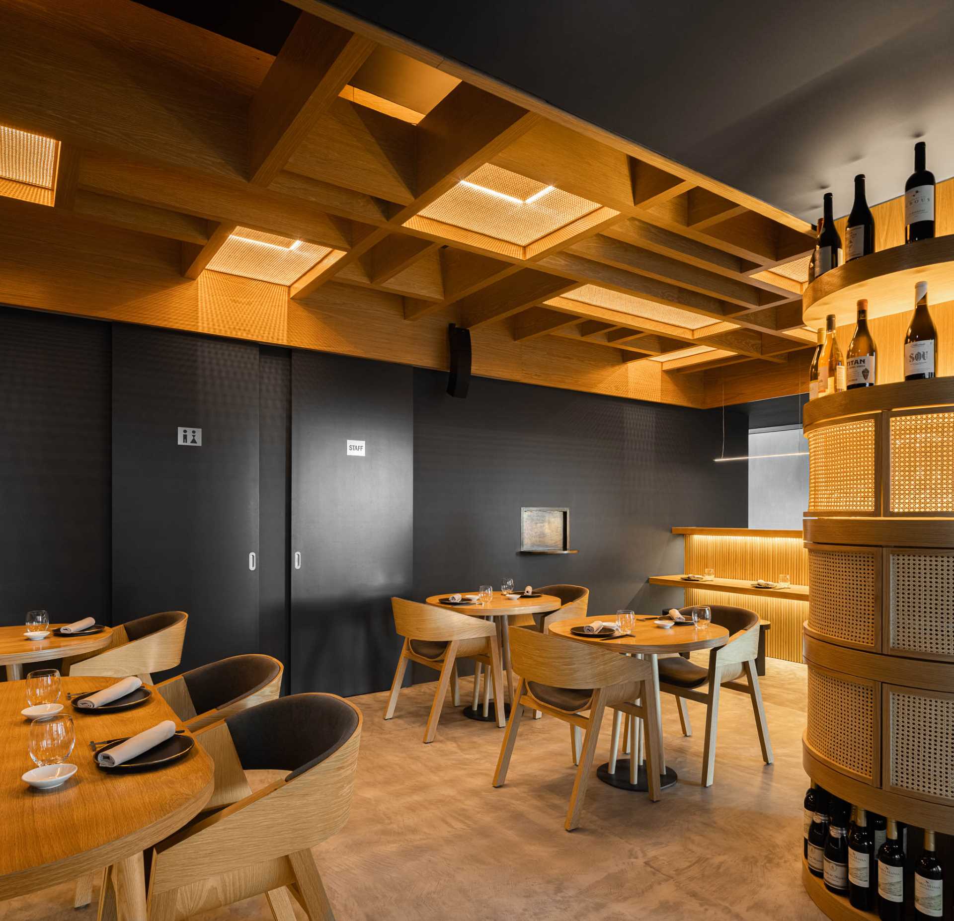 A modern restaurant interior with dark walls, wood accents, and straw panels.