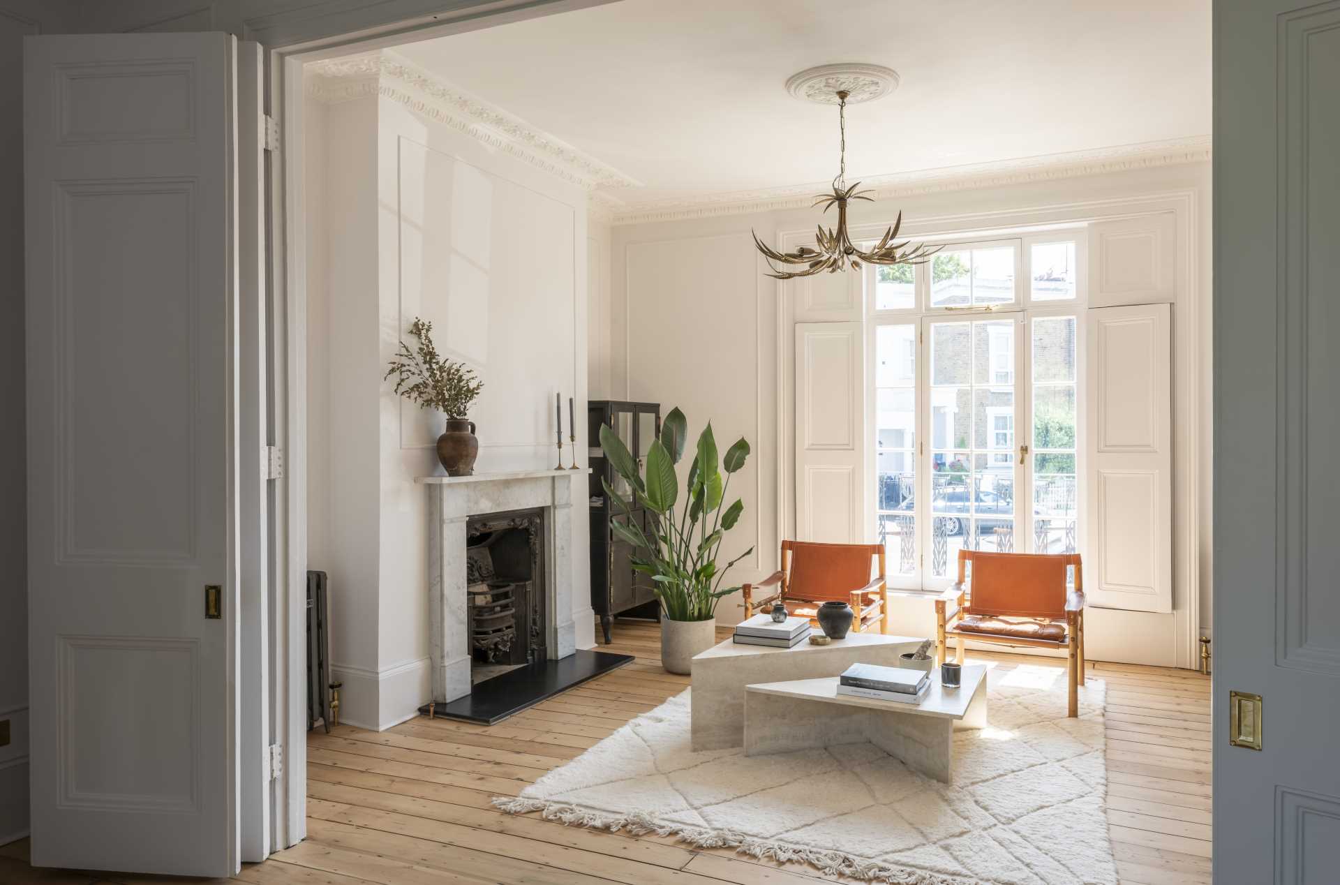 A living room with wood floors, a fireplace, and large windows that look out onto the street.