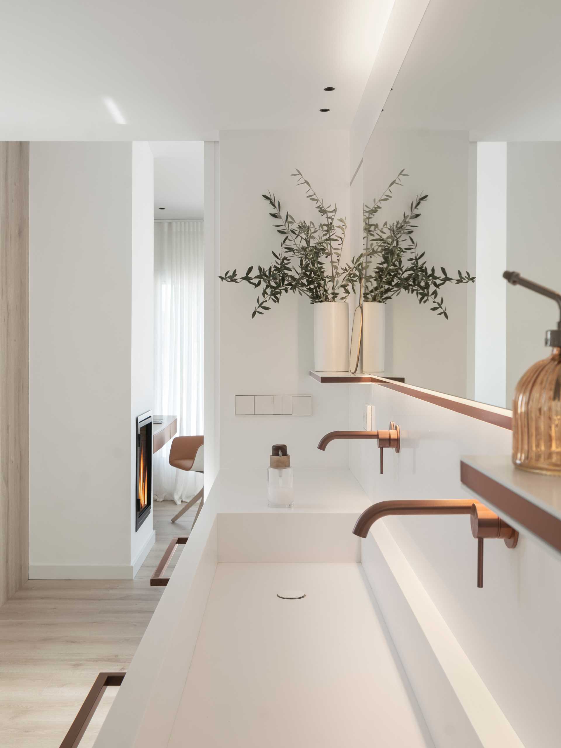 Using Corian White, this modern bathroom includes a long vanity, with a trough sink, LED lighting, and copper accents.