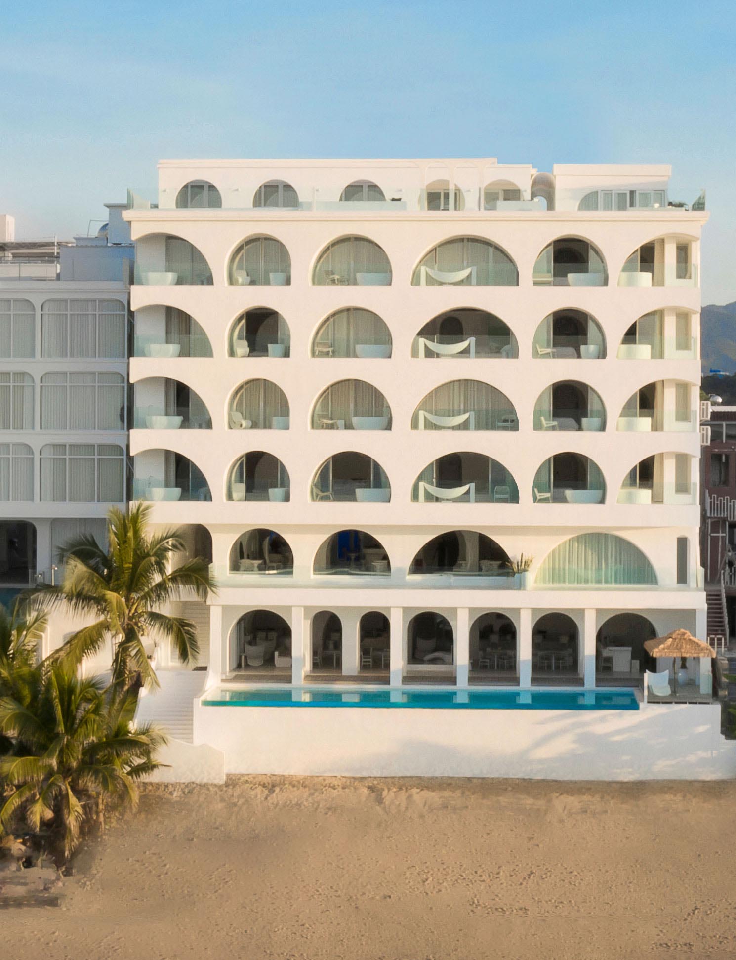 A modern hotel with a white exterior that includes arches of different shapes.