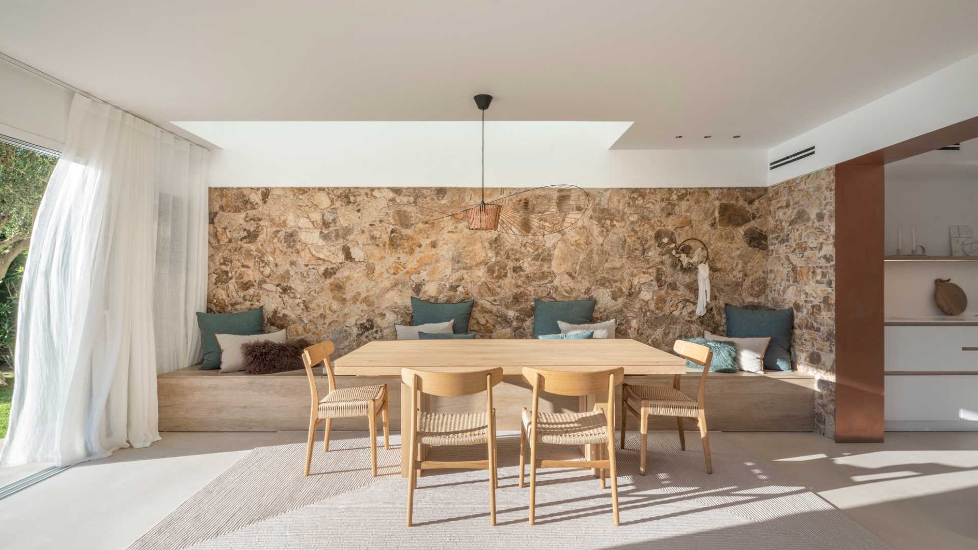 A modern dining room with a skylight, a stone accent wall, and a long built-in bench that acts as seating for the dining table.