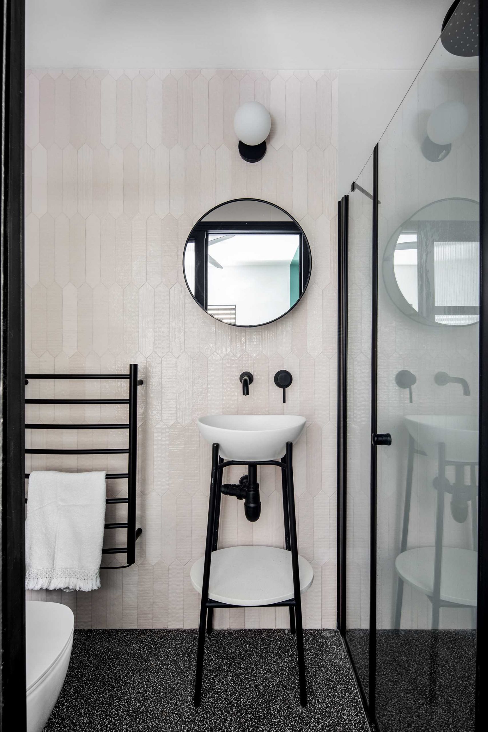 This modern bathroom includes hexagonal elongated pale pink tiles, while the flooring consists of small black and white terrazzo tiles