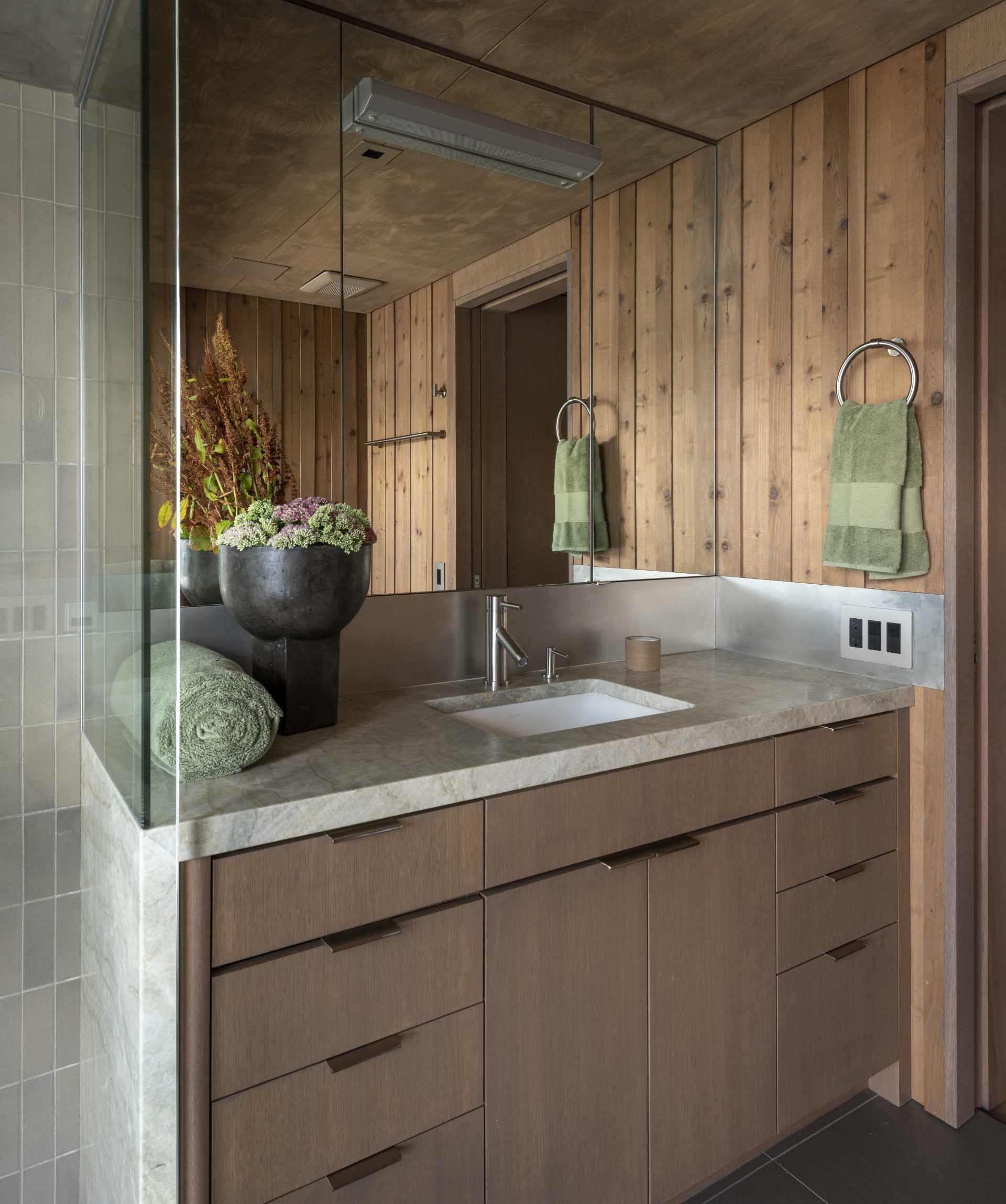 This primary bathroom features wood walls, while the dual shower has water views and tiled walls.