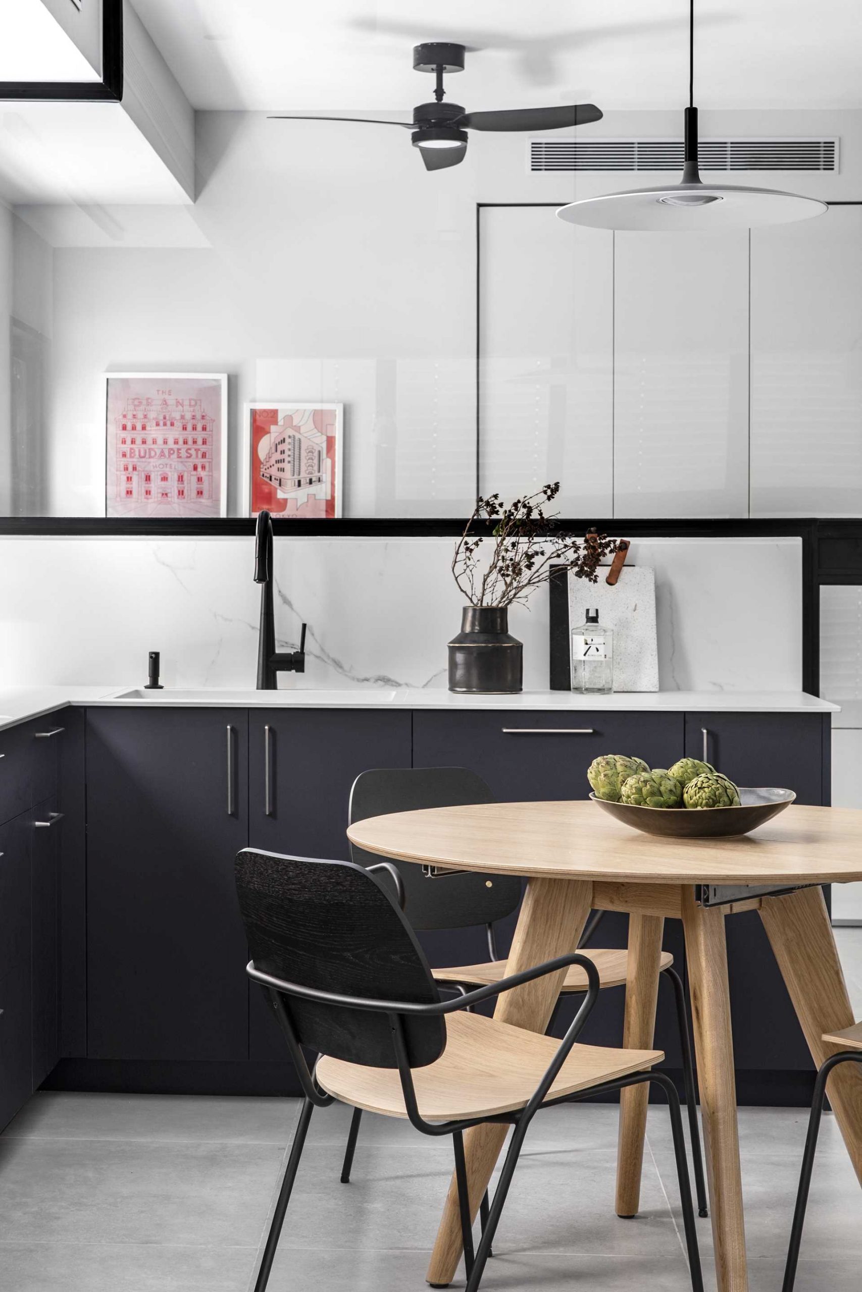 A modern black kitchen with white countertops and a glass wall.