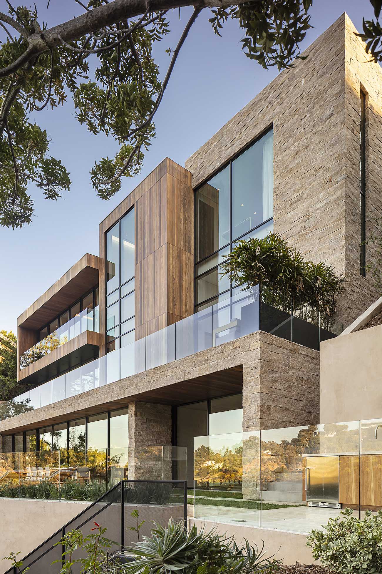 A modern house with multiple levels is clad in limestone, wood, and glass.