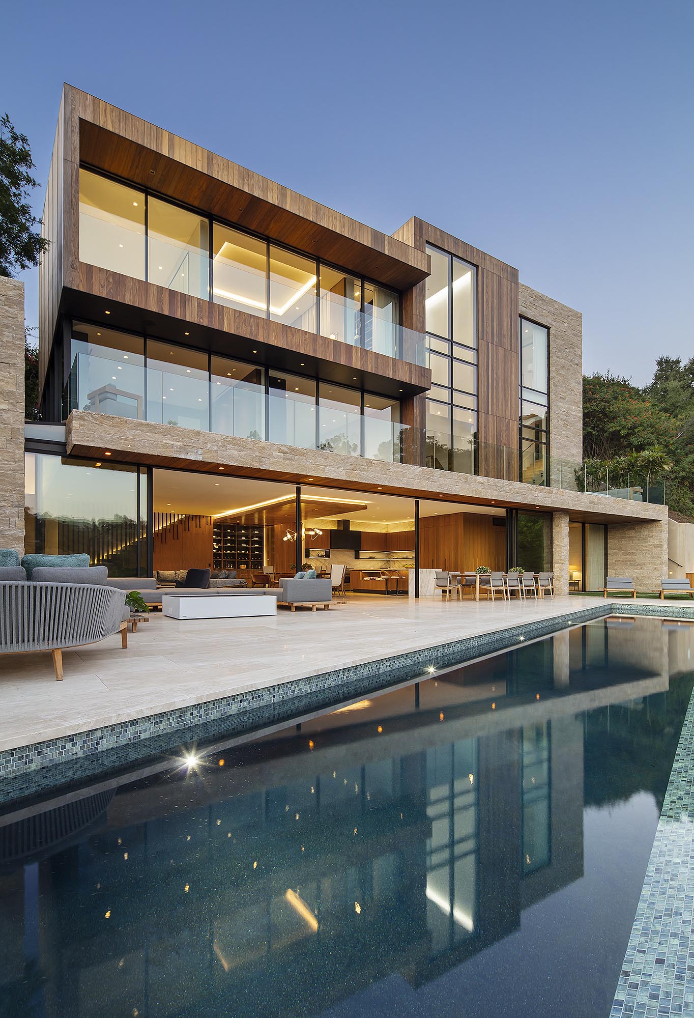 A modern house has oversized sliding glass doors that open to a large patio, outdoor kitchen, and swimming pool.