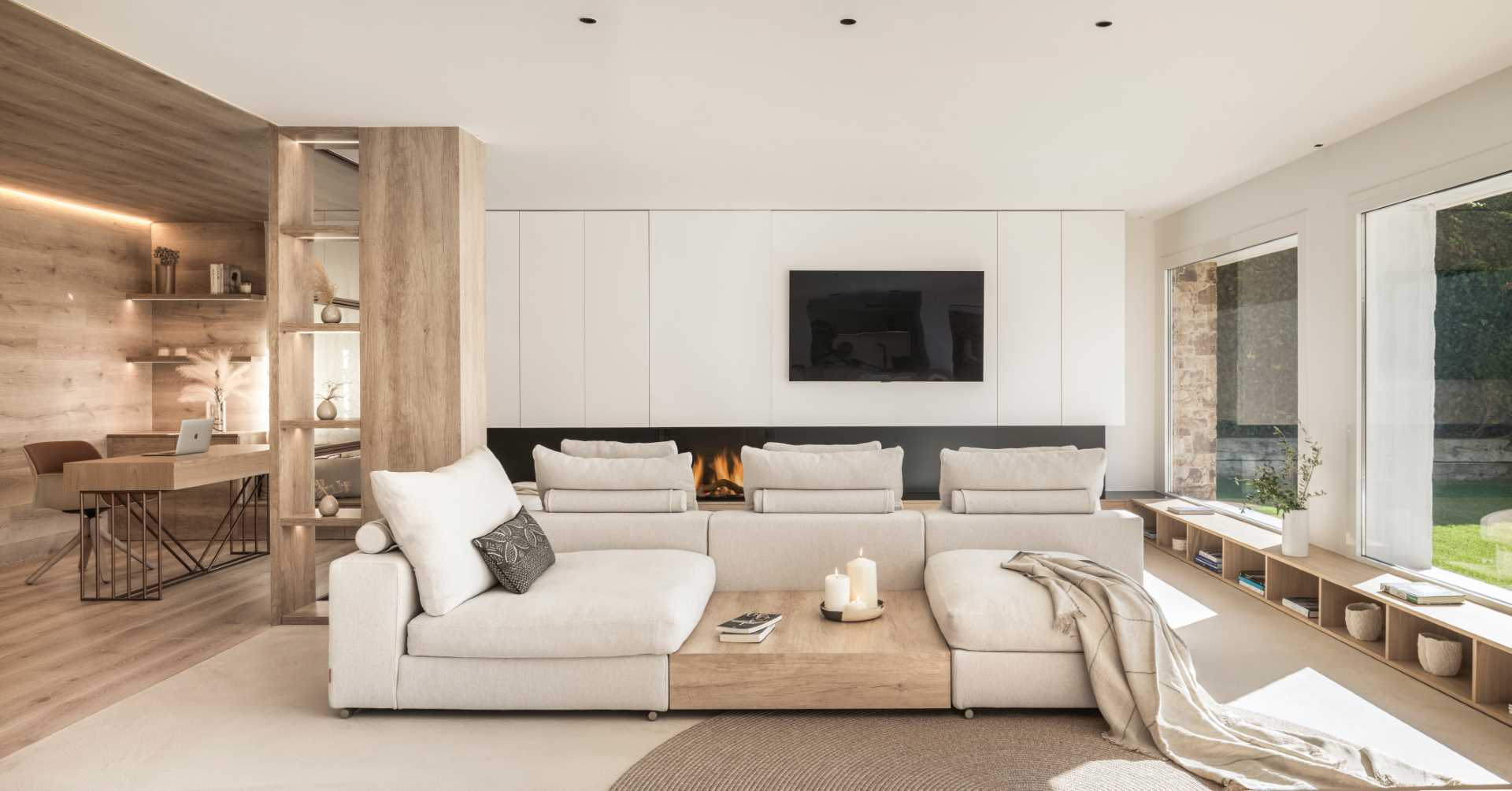 In this modern living room, a square sofa takes center stage, while a custom designed storage unit runs underneath the windows, and meets up with the hearth of the fireplace.