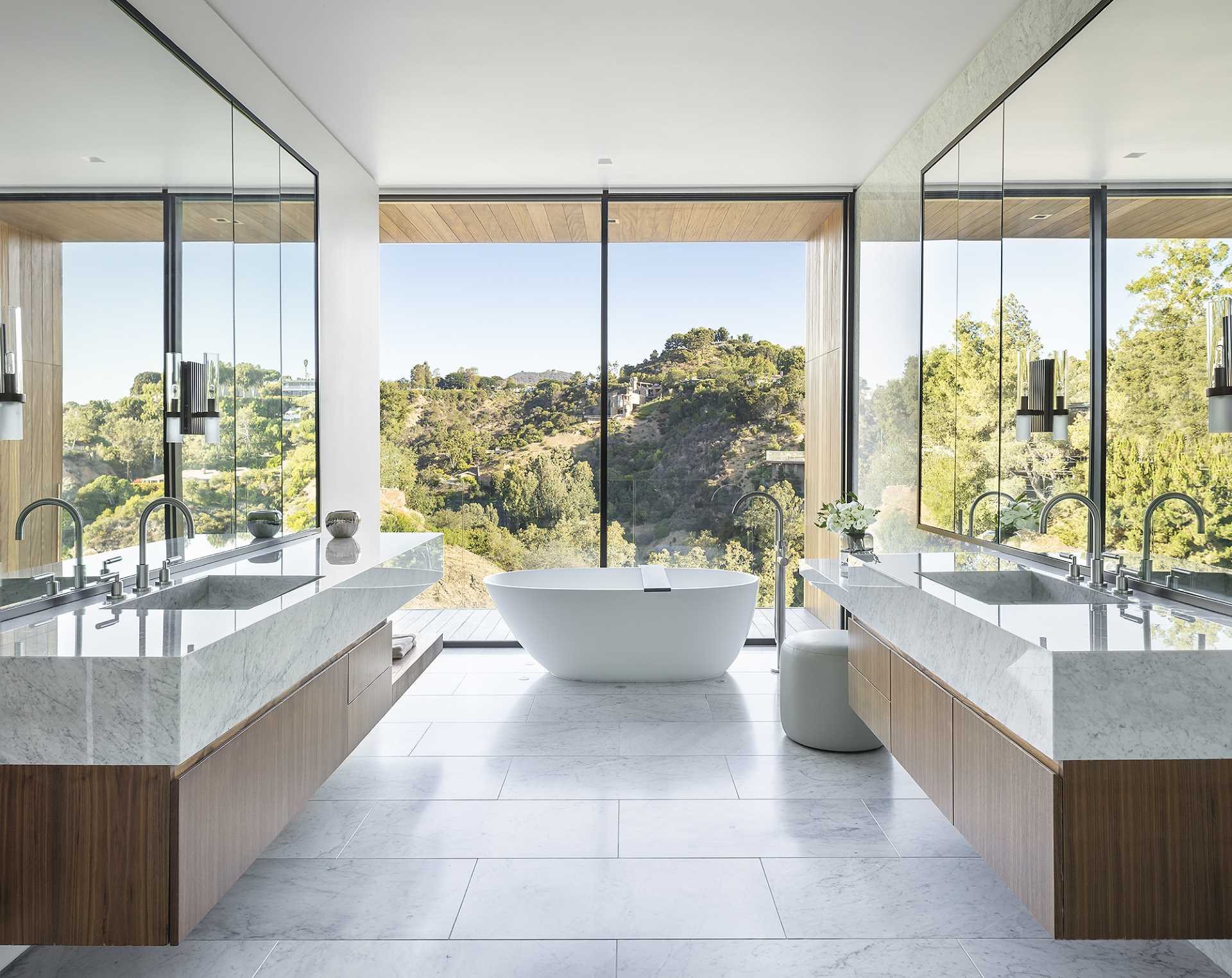 In this modern primary bathroom, floor to ceiling windows provide valley views from the bathtub, while the floating dual vanities are located on either side of the room.