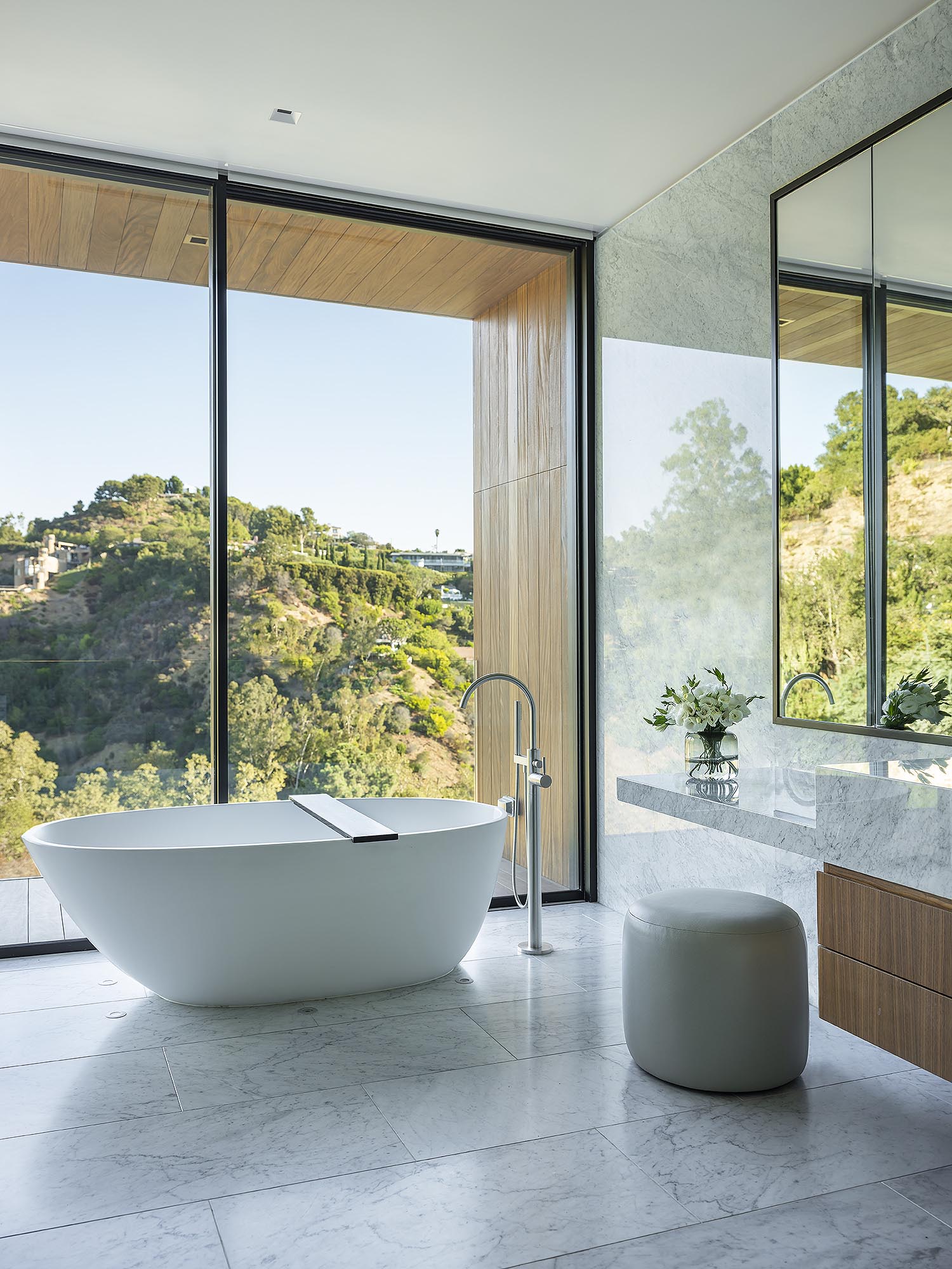 A modern bathroom with floor to ceiling windows, floating vanities, and a freestanding bathtub.