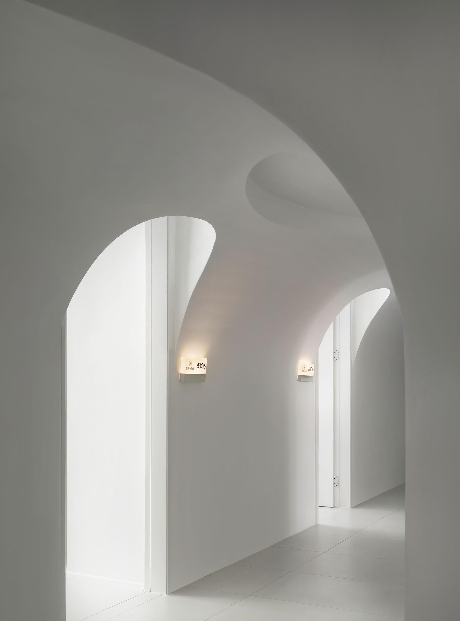 A modern hotel hallway with white walls and arched entryways.