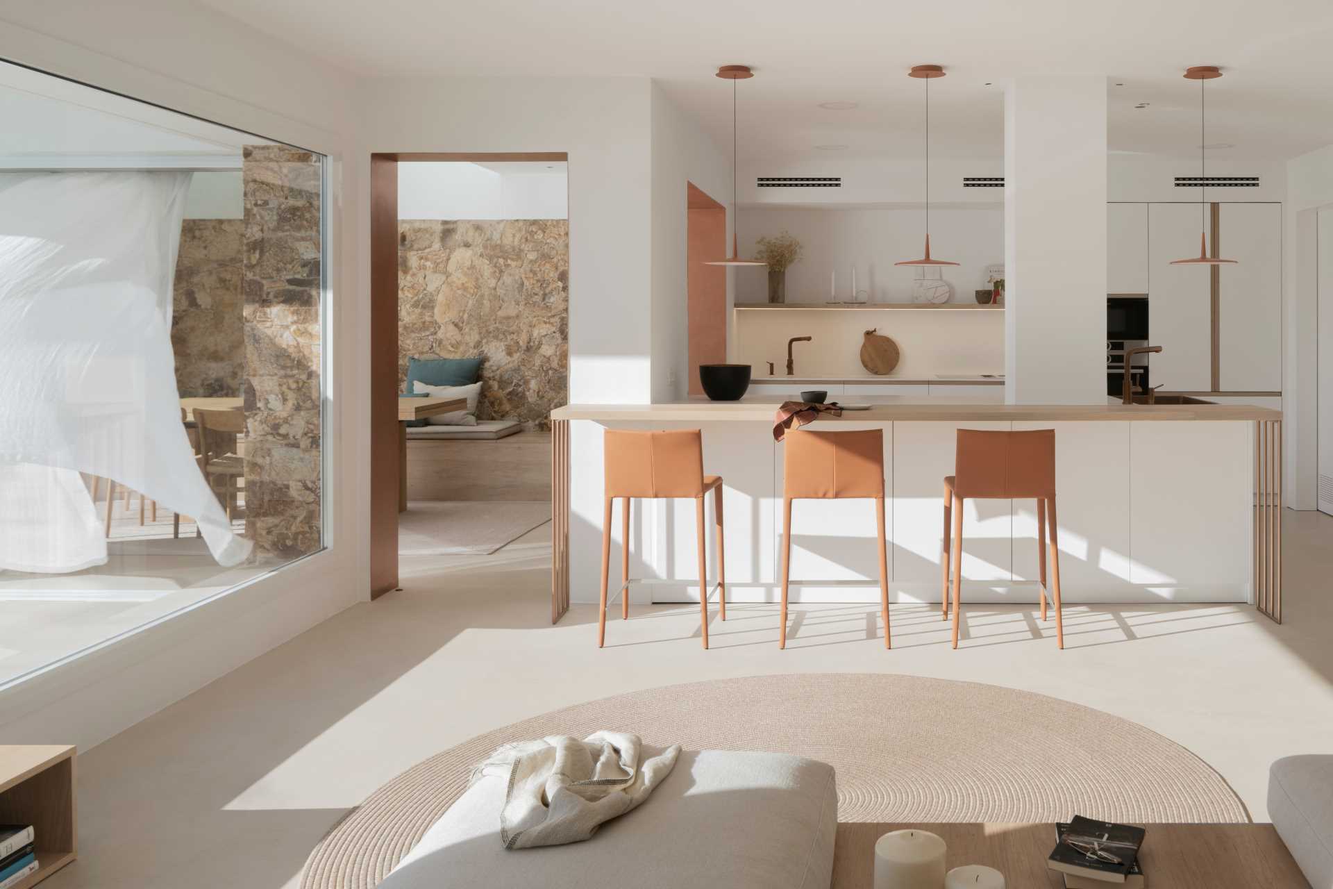A modern kitchen with a white and copper color palette, and a long breakfast bar.