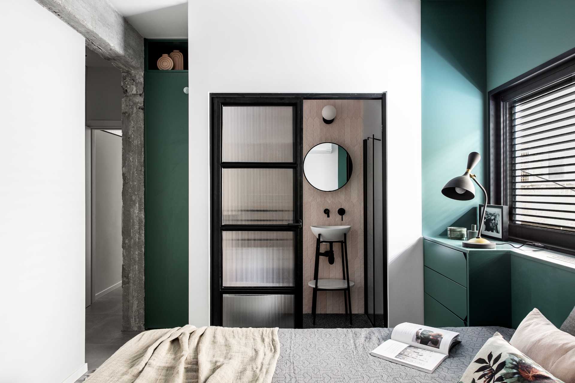 A modern bedroom with green accent walls and an ensuite bathroom.