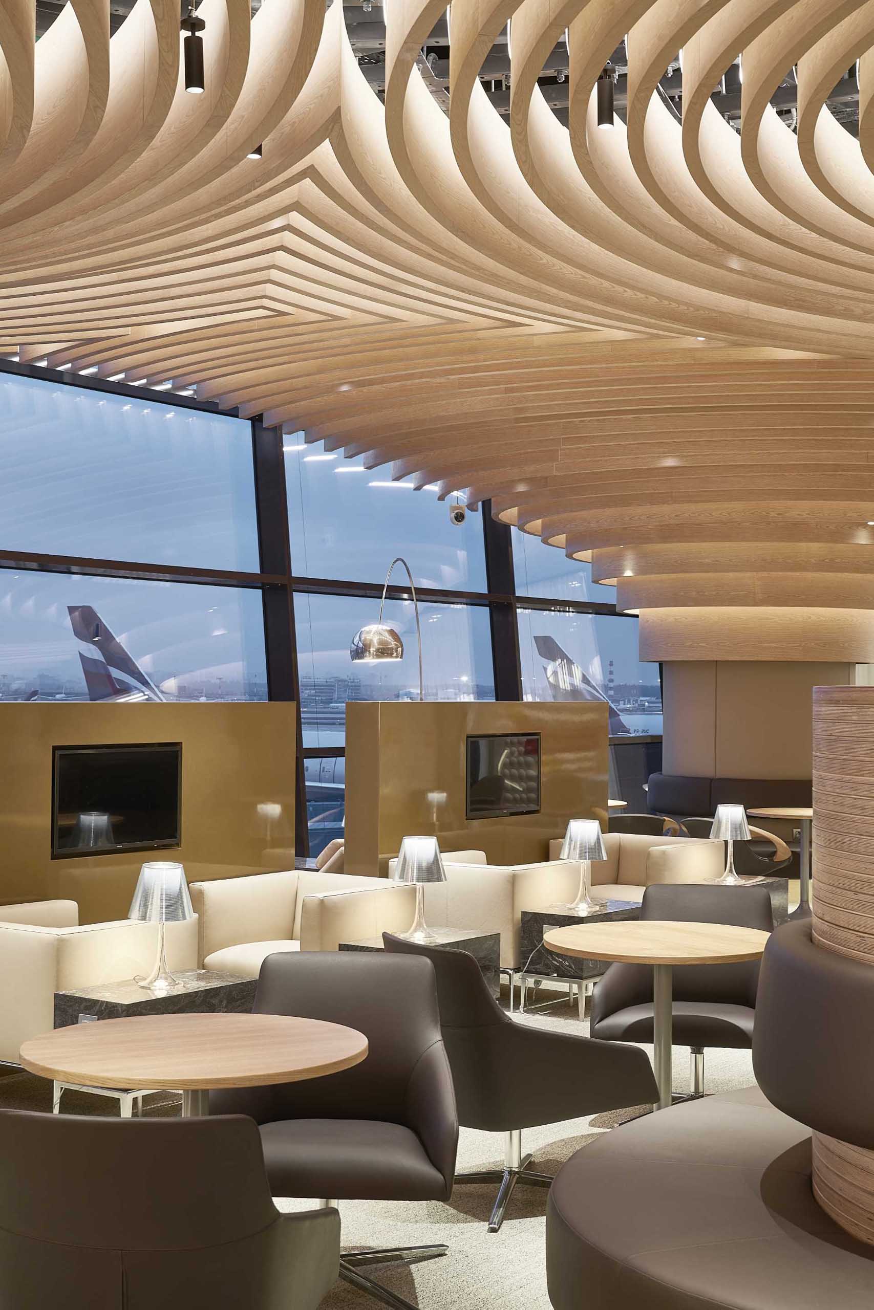 A modern airport lounge with circular wood ceiling patterns.