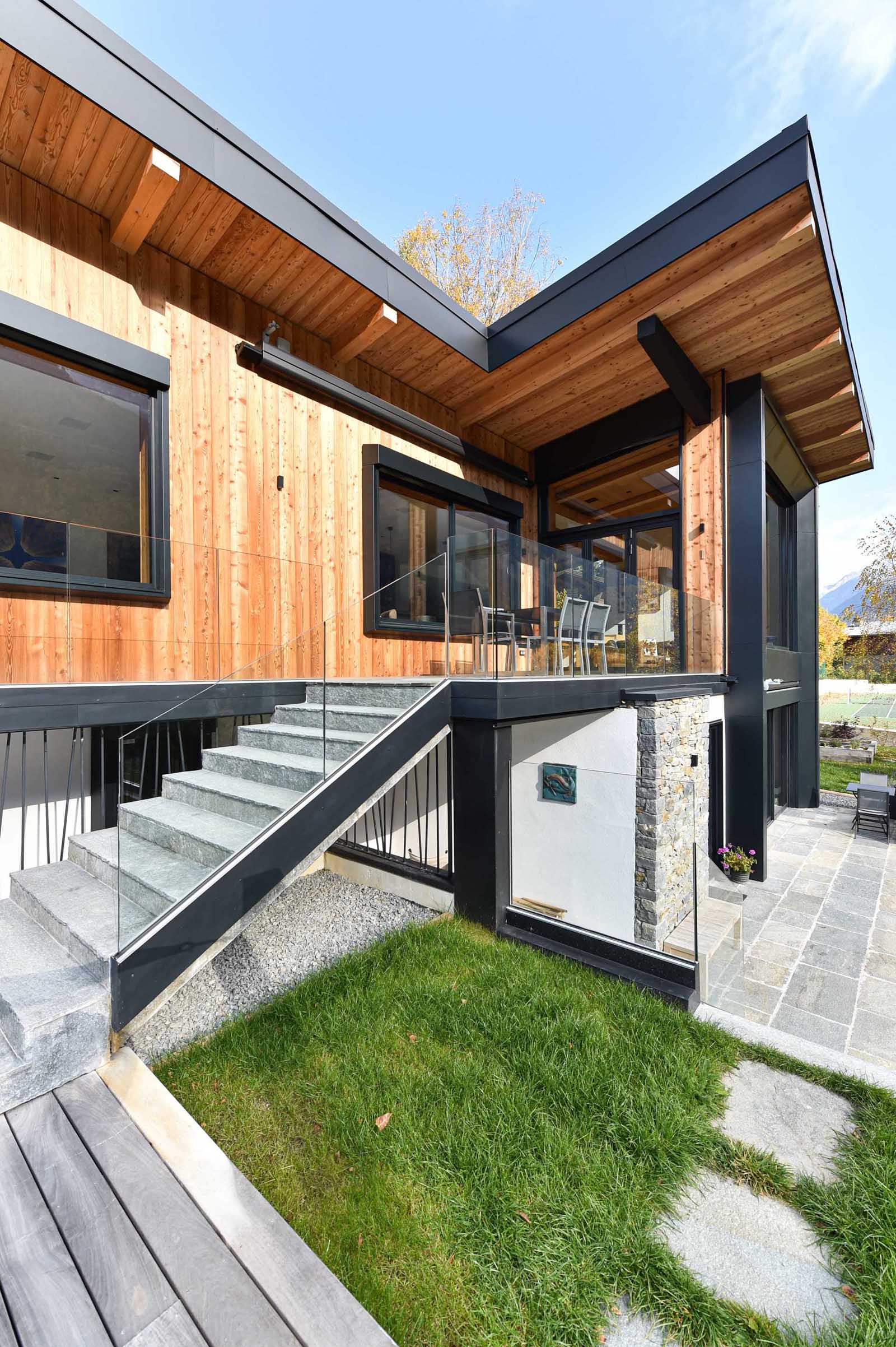 A modern home with wood siding, black accents, and stairs with glass railings.