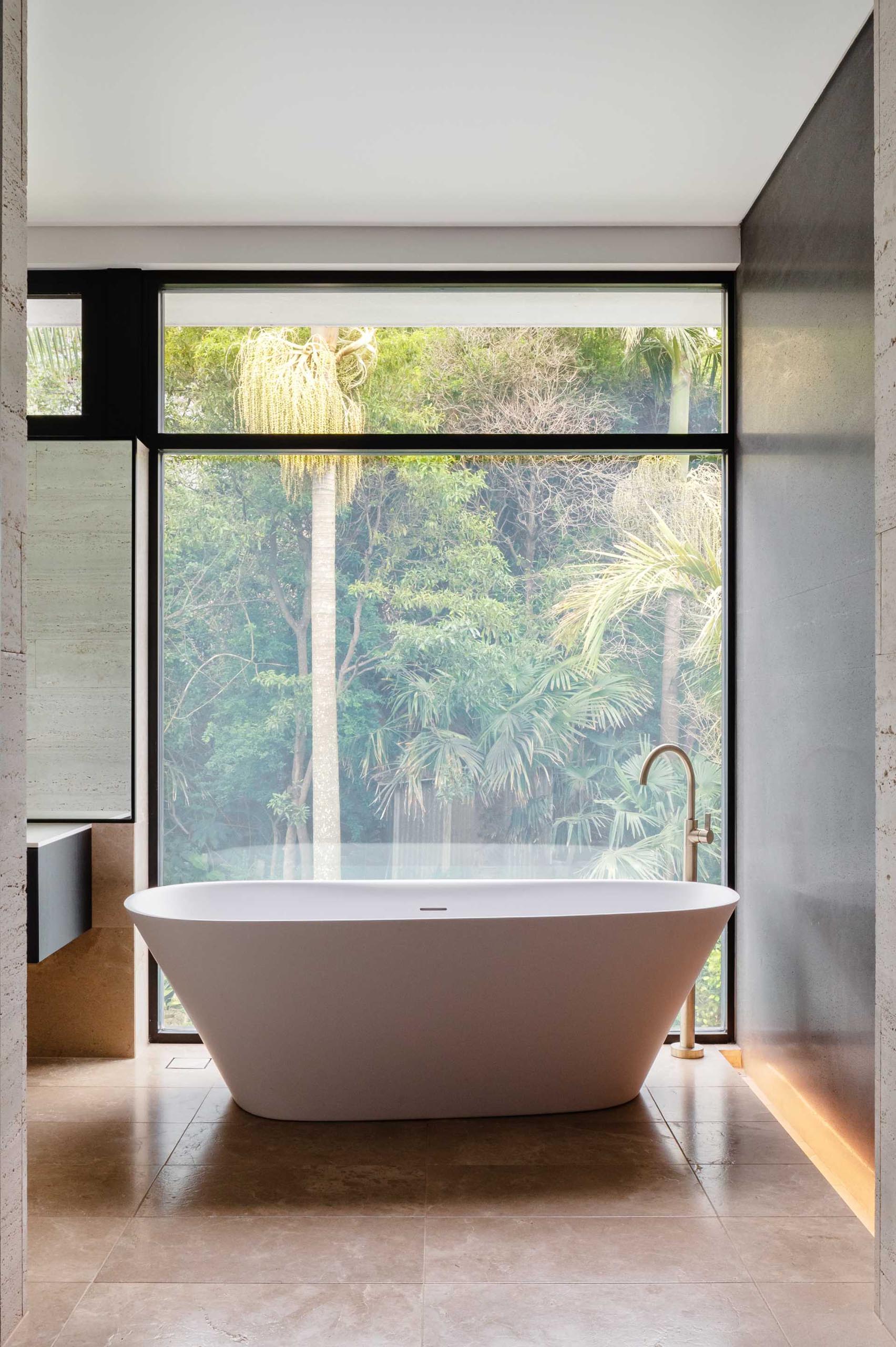 In this modern bathroom, a freestanding bathtub has been placed in front of a window that overlooks the backyard.