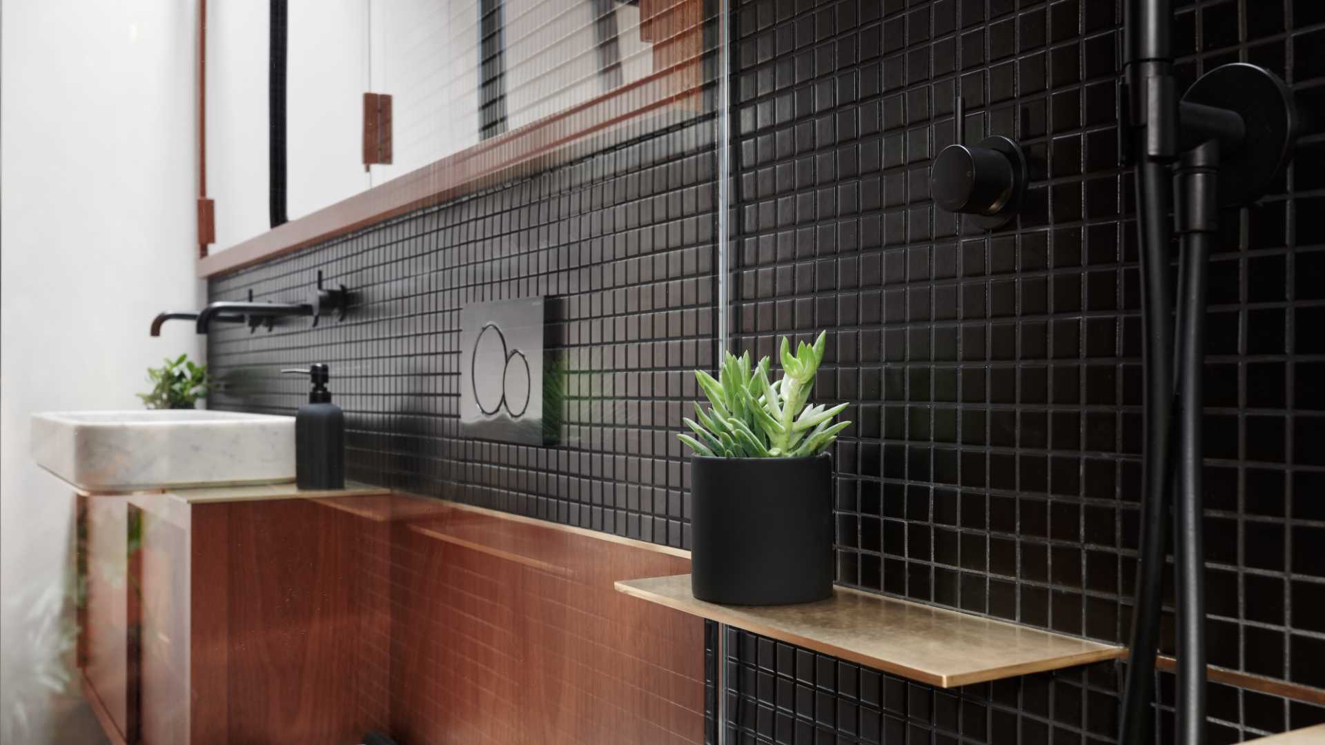 A modern bathroom with wood vanity and black tiles.