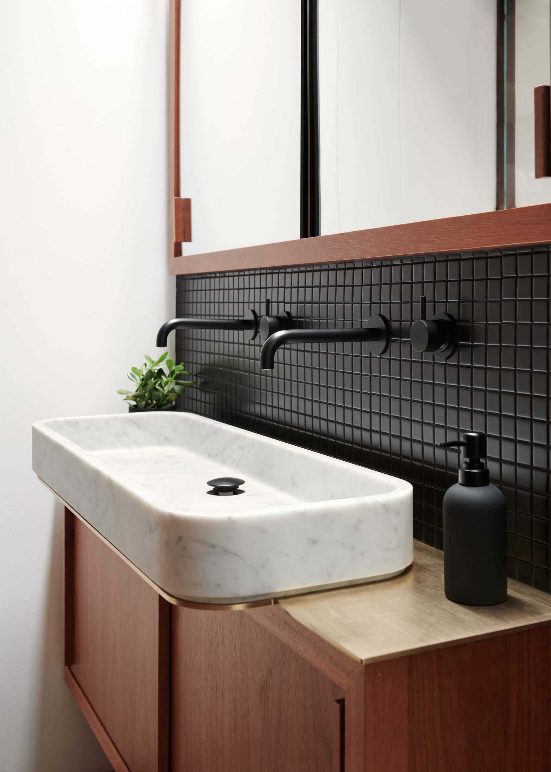 A modern wood vanity with black tiles and matching matte black hardware.