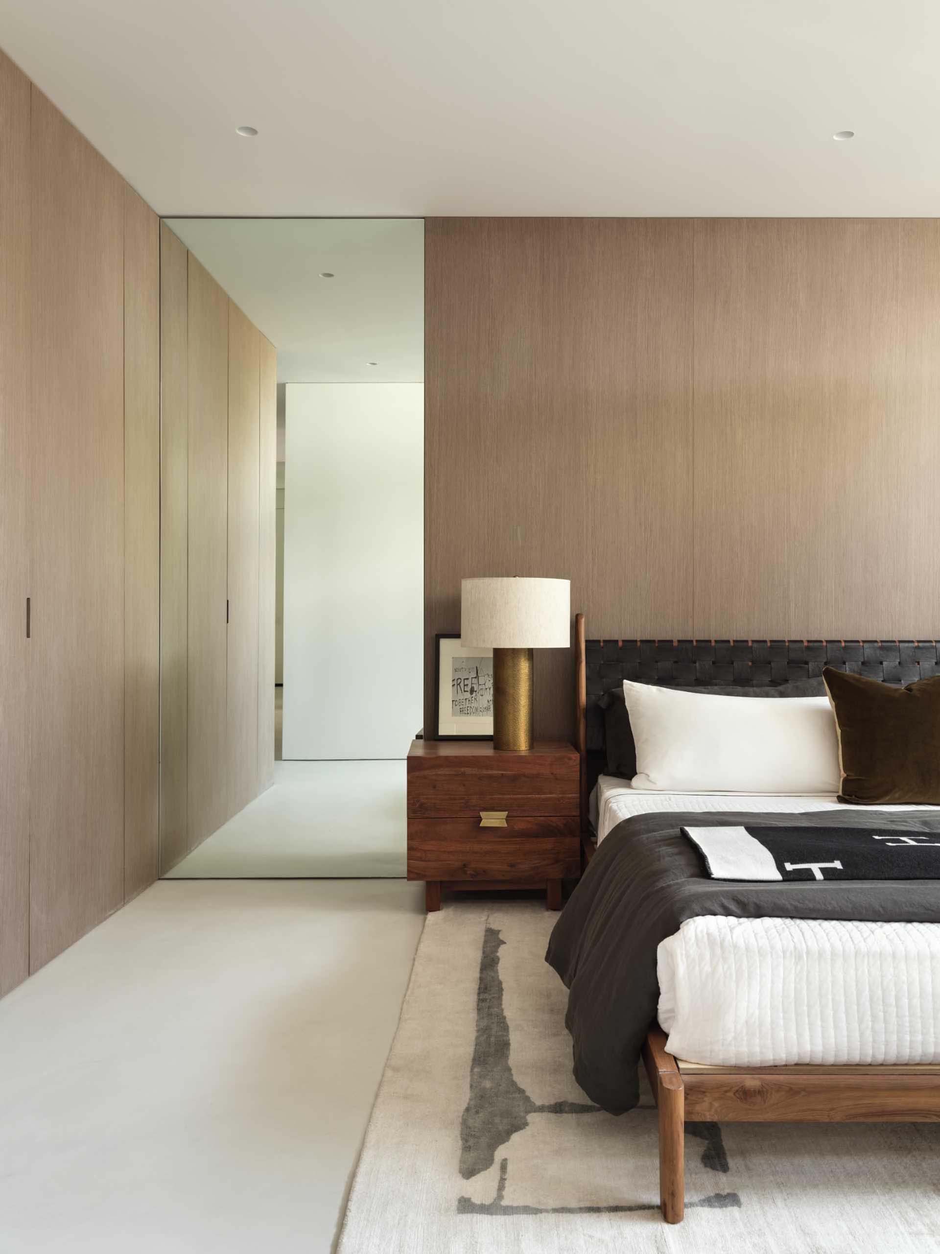A modern bedroom with a wood accent wall and floor to ceiling mirror.