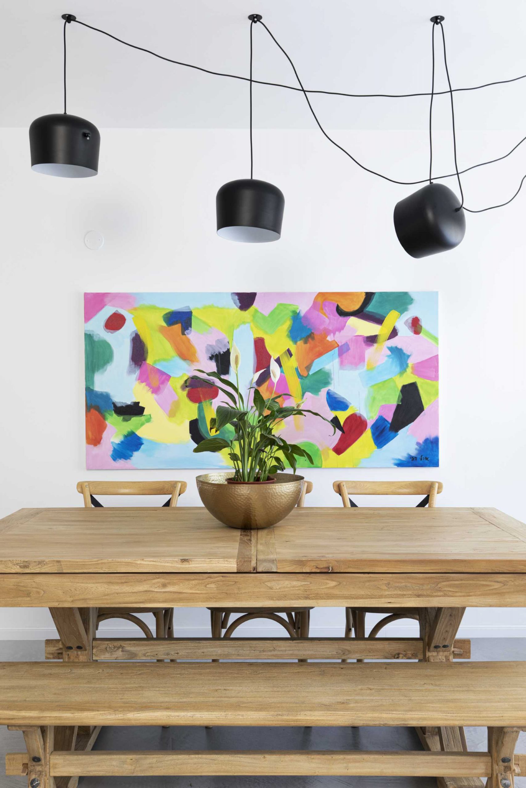 A modern dining room with a wood table, black lighting, and colourful artwork.