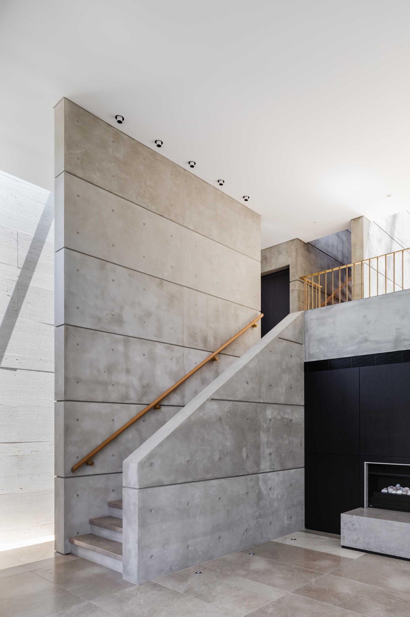 A modern home with concrete walls, limestone tiled floors, and a wood handrail.