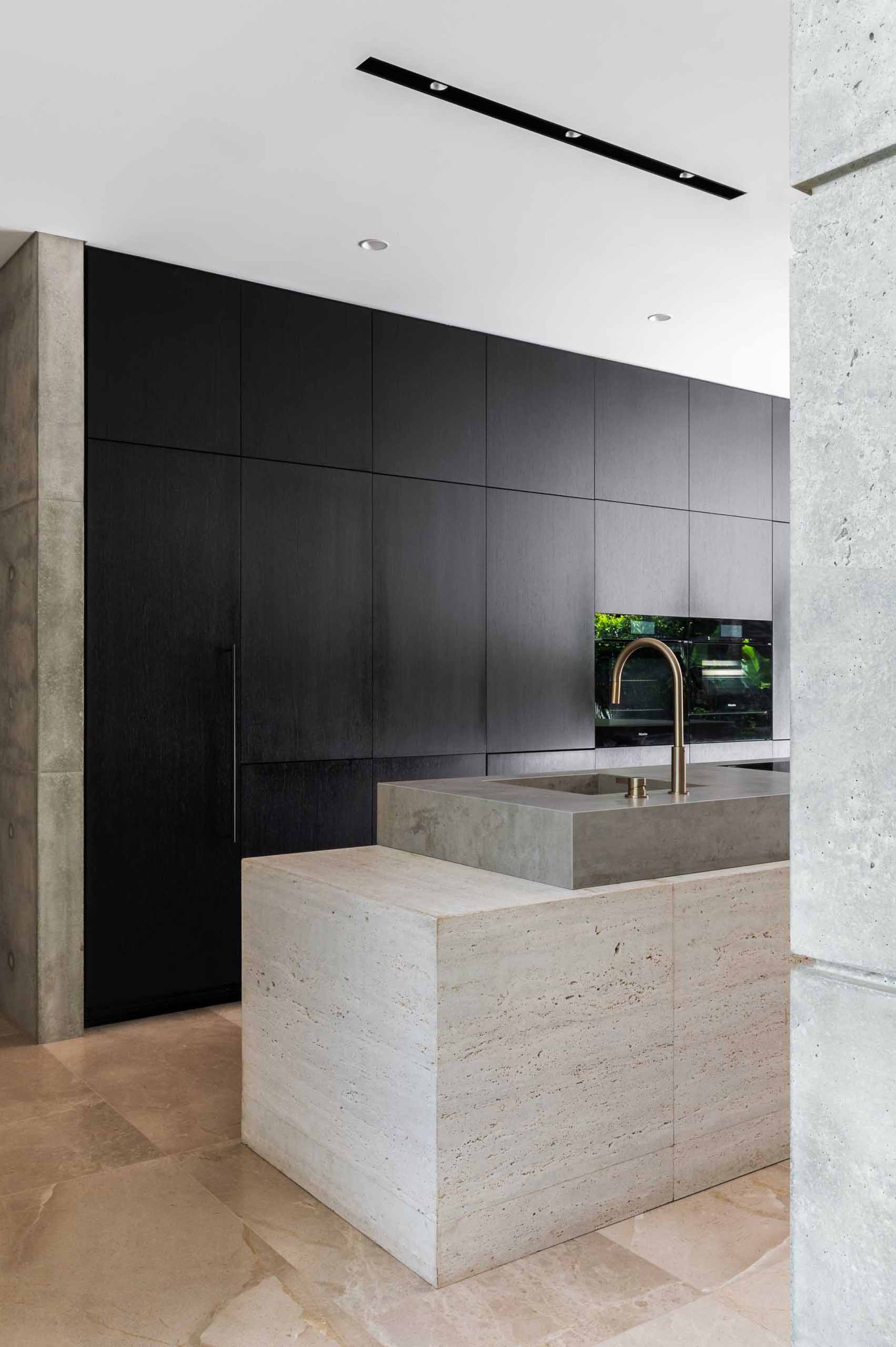 This minimalist kitchen features concrete walls, limestone tiled floors, sandblasted travertine wall cladding, and minimalist black cabinets