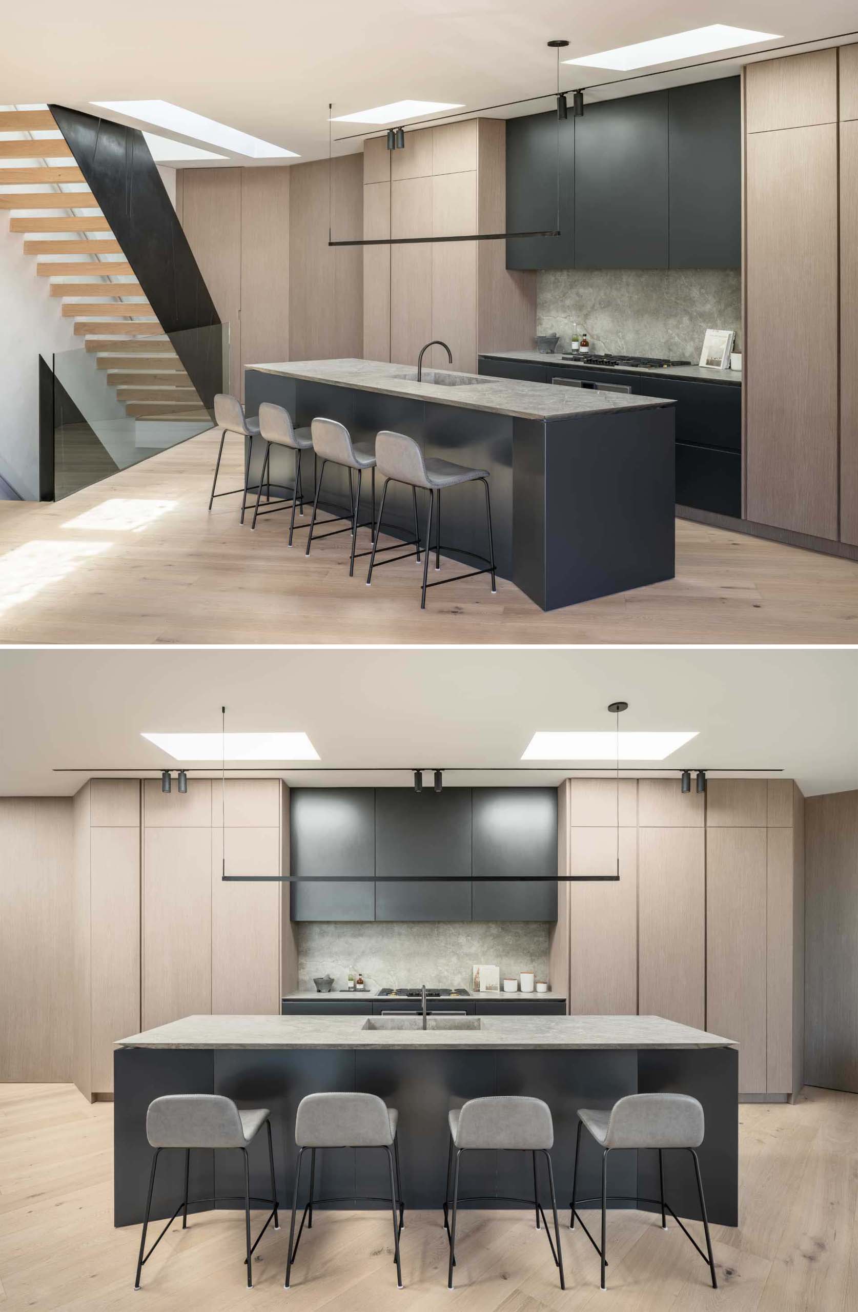 In this modern kitchen, the island provides workspace and an informal cantilevered seating area, while the minimalist light fixture above the island complements the black cabinetry and nearby stairs.