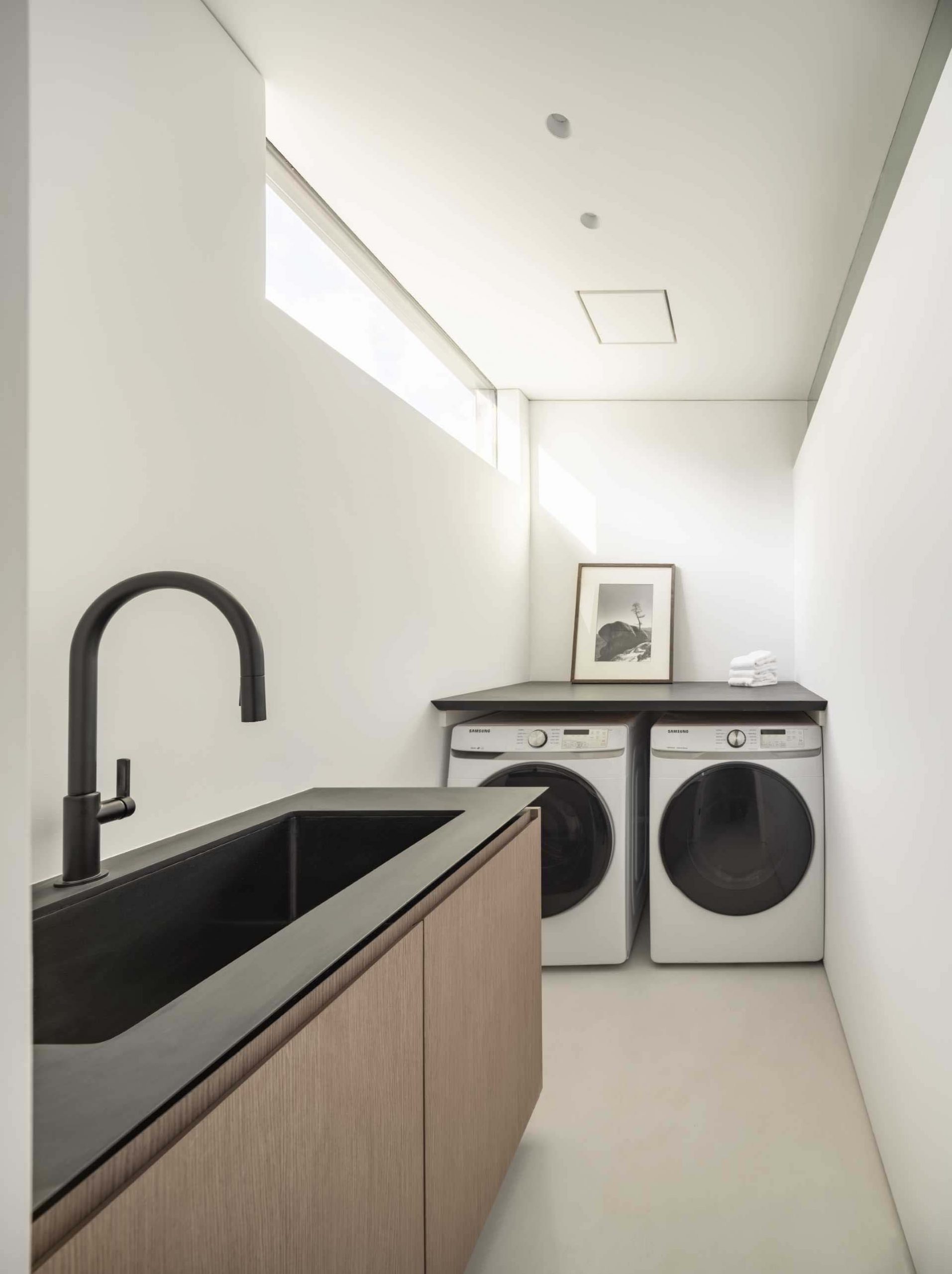 In this modern laundry room, the washing machine and dryer are positioned below a counter that adds a workbench to the space.