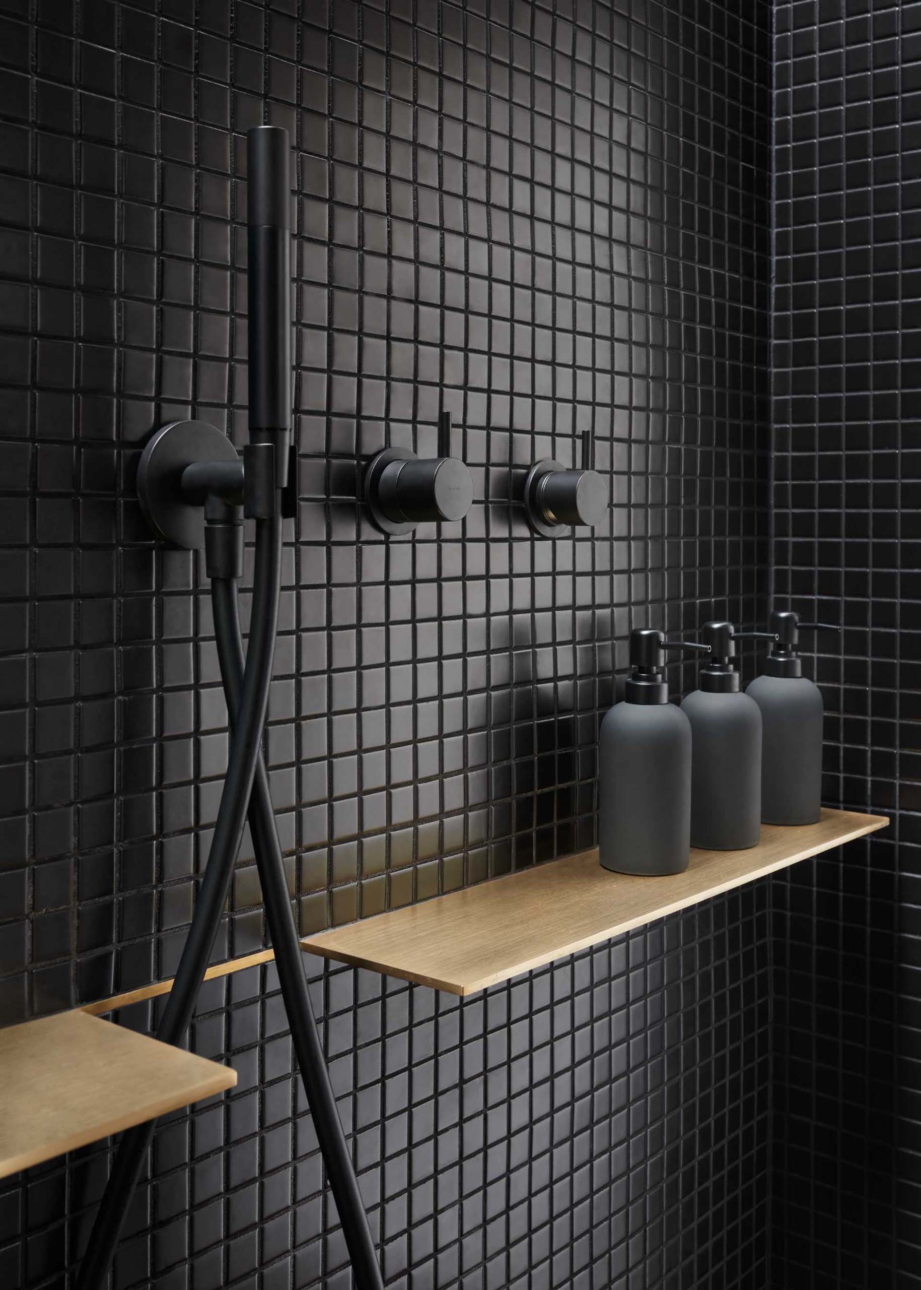 A modern bathroom with matte black plumbing fixtures and black tiles.