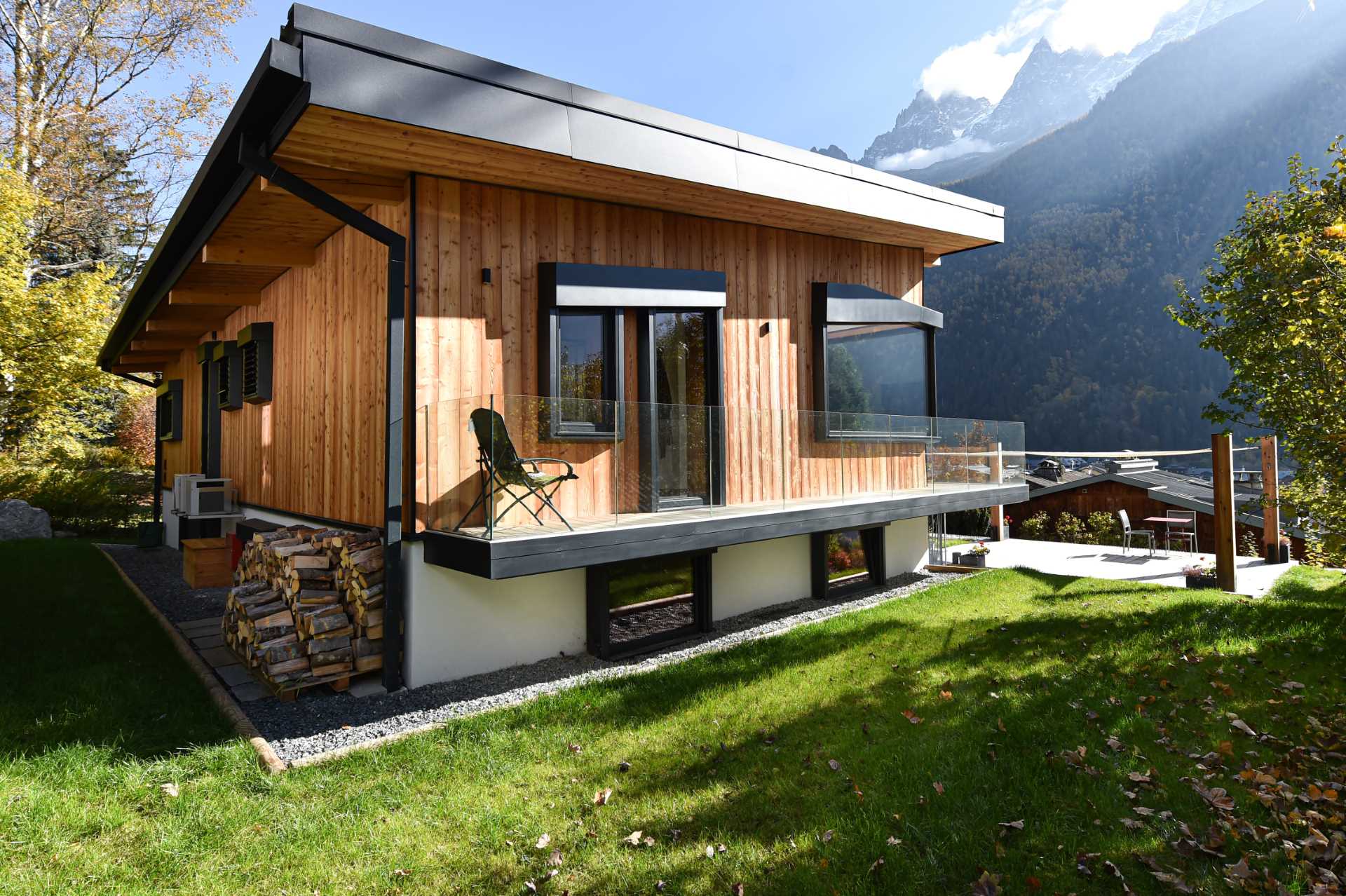 A modern home with wood siding, black window frames, and a wrap-around balcony with glass railing.