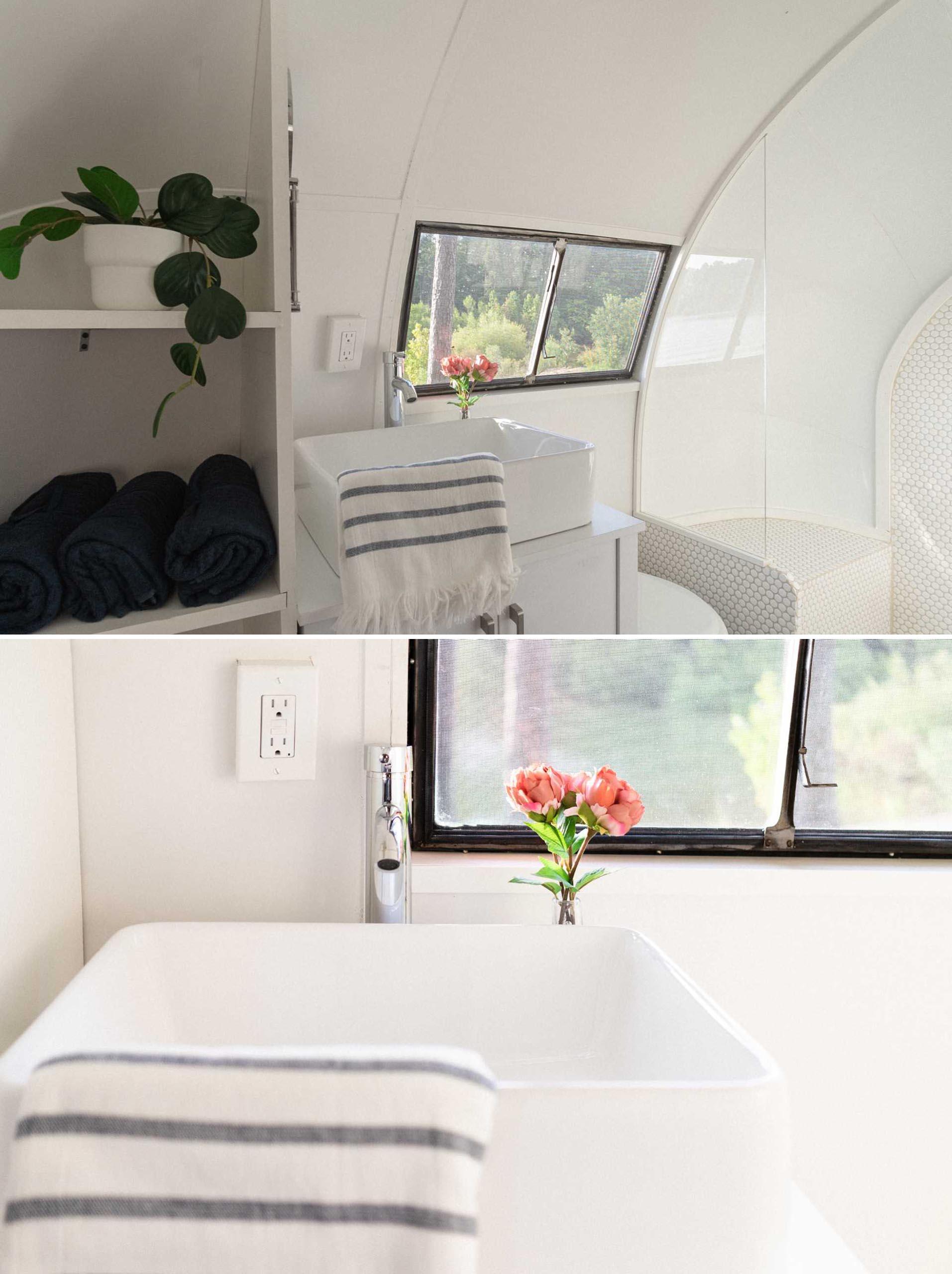 This remodeled vintage travel trailer includes a spa-inspired bathroom, with shelving, a vanity, toilet, and a shower.