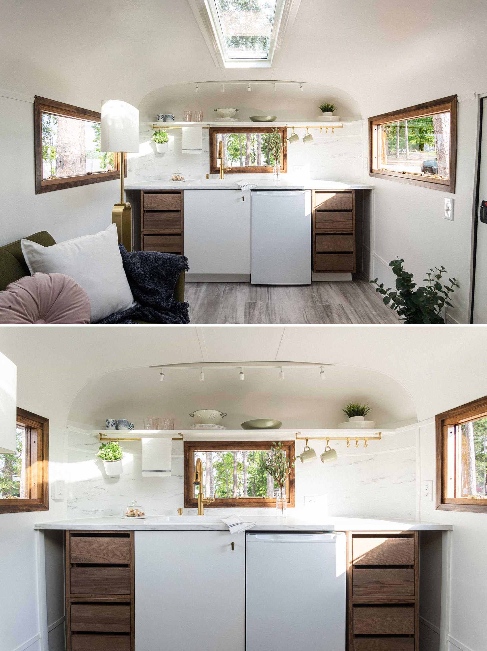 The remodeled kitchen of this vintage travel trailer includes wood cabinetry, a shelf, and a light colored countertop.