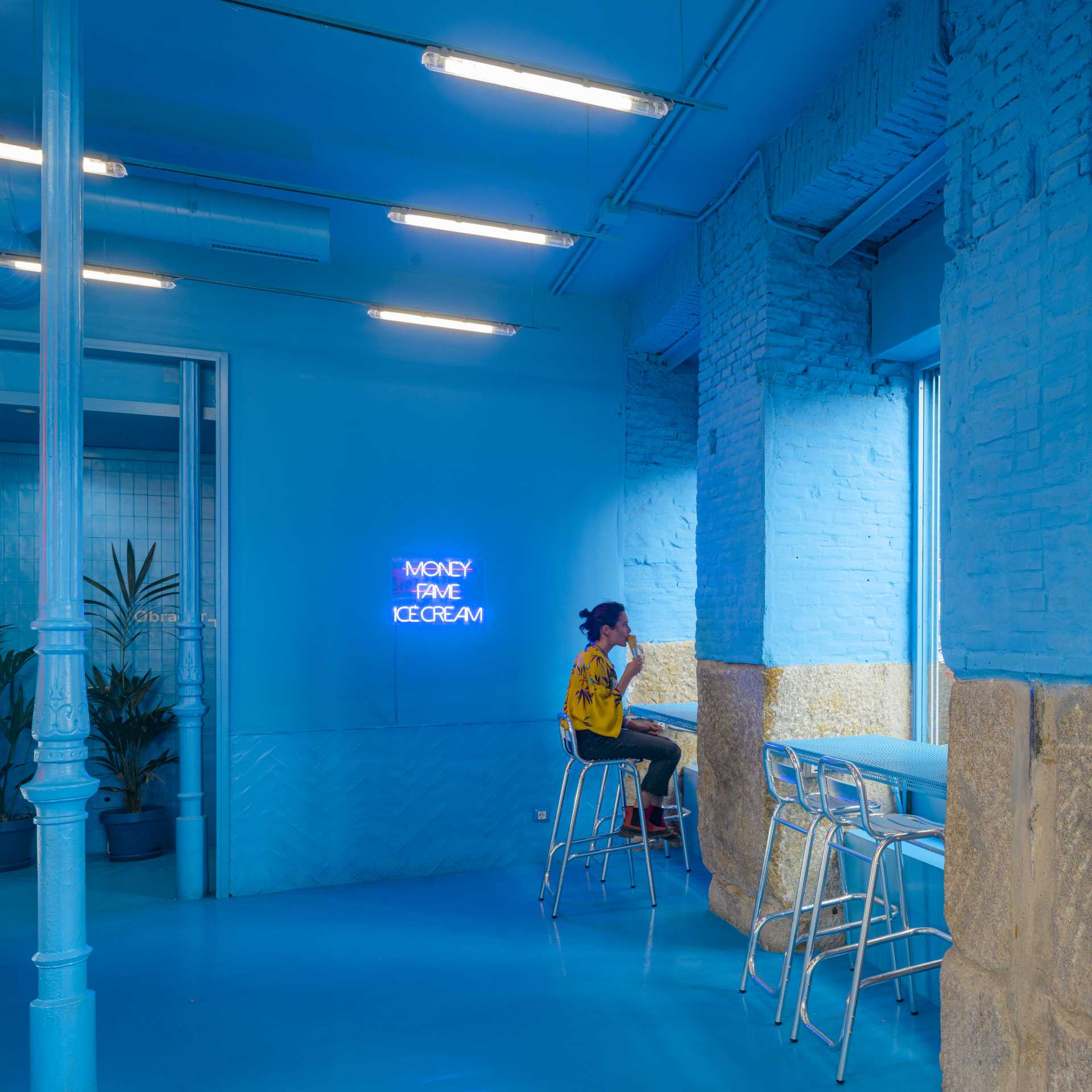 A modern ice cream shop with a blue interior has seats by the windows.
