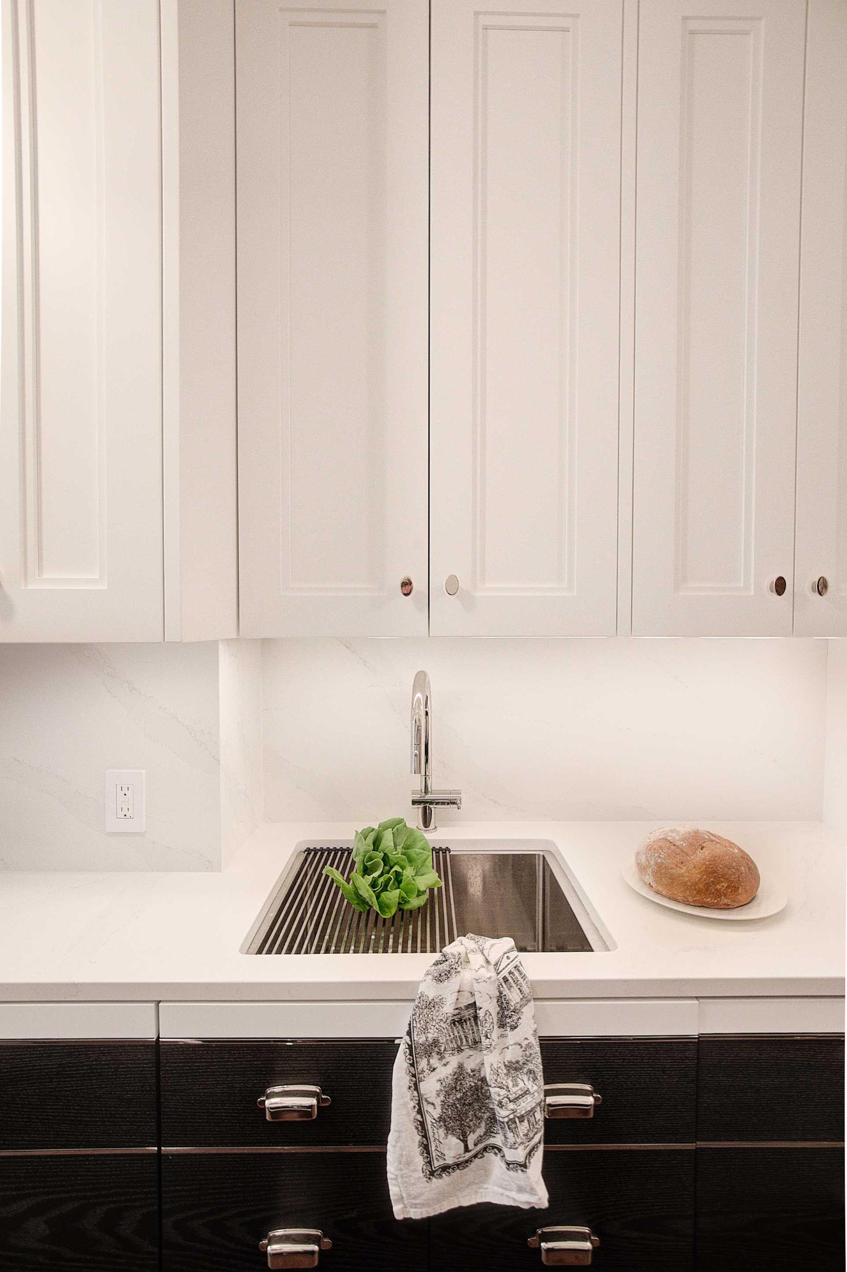 A contemporary kitchen with a stainless steel sink and drying rack, white upper cabinets, and black lower cabinets.